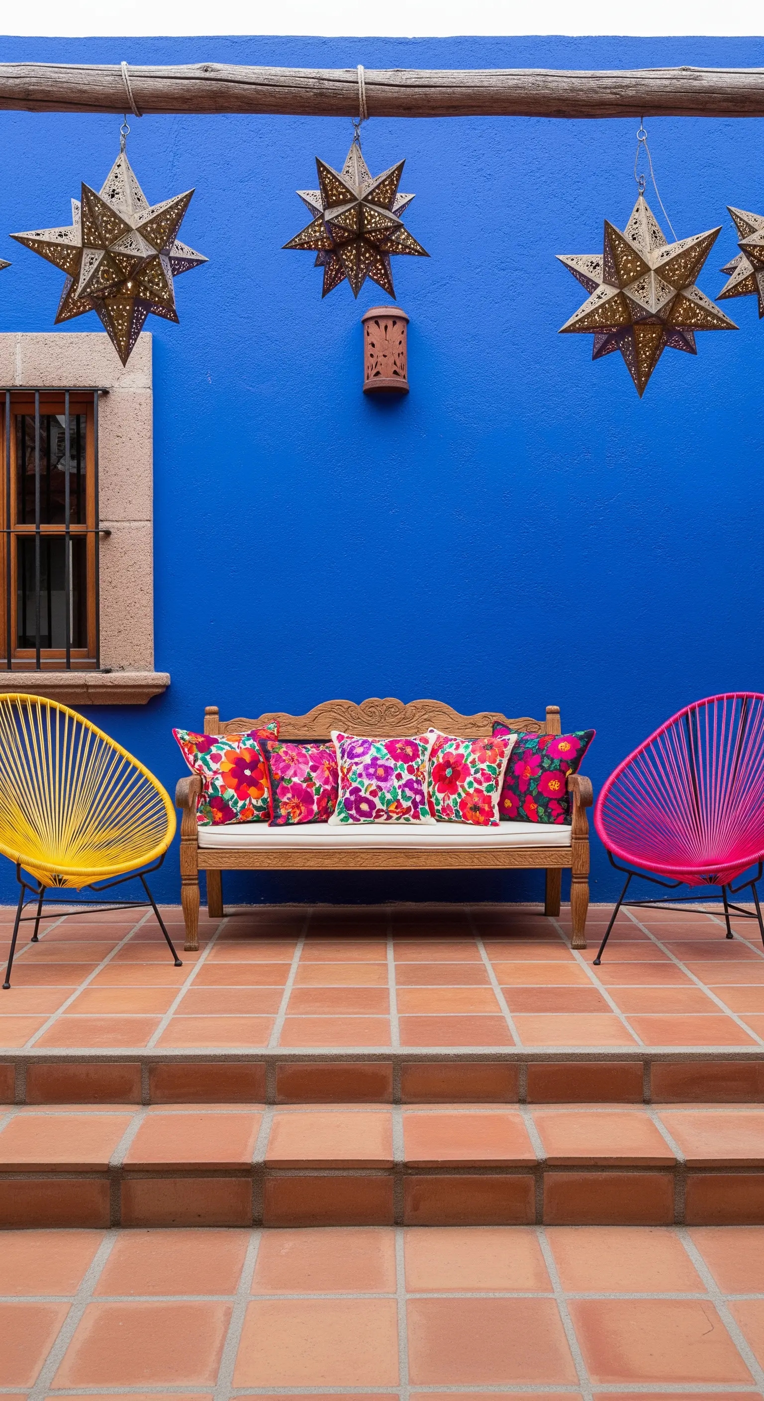 Patio con parete blu intenso, sedie Acapulco gialla e fucsia e lanterne a stella.