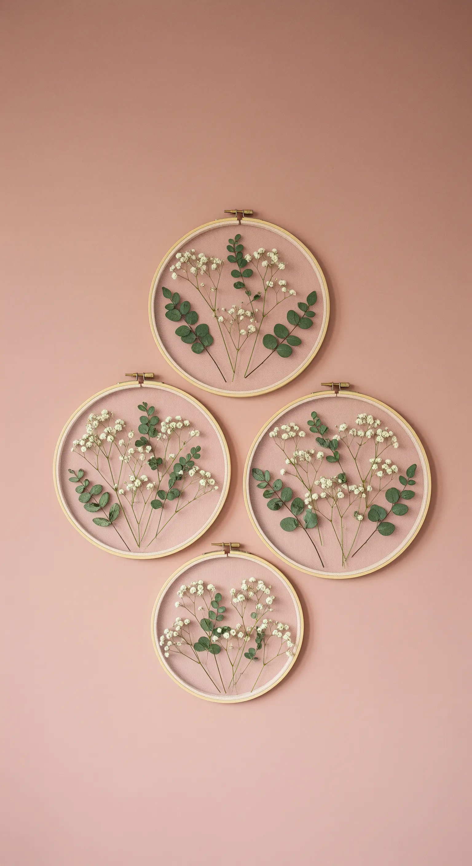Quattro telai da ricamo con tulle e fiori secchi appesi a una parete rosa.