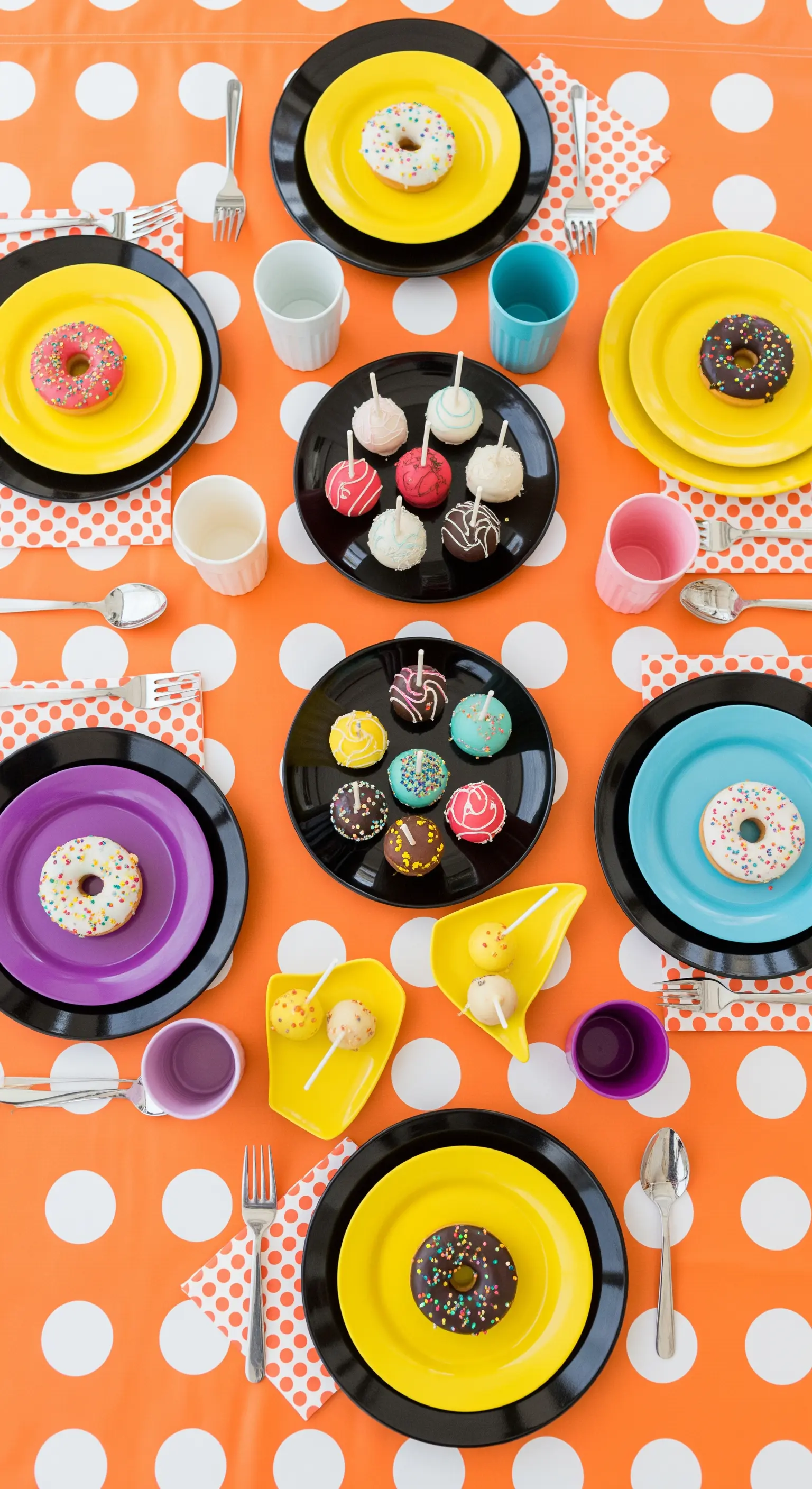 Tavola a pois arancioni e bianchi con piatti colorati, ciambelle e cake pop.