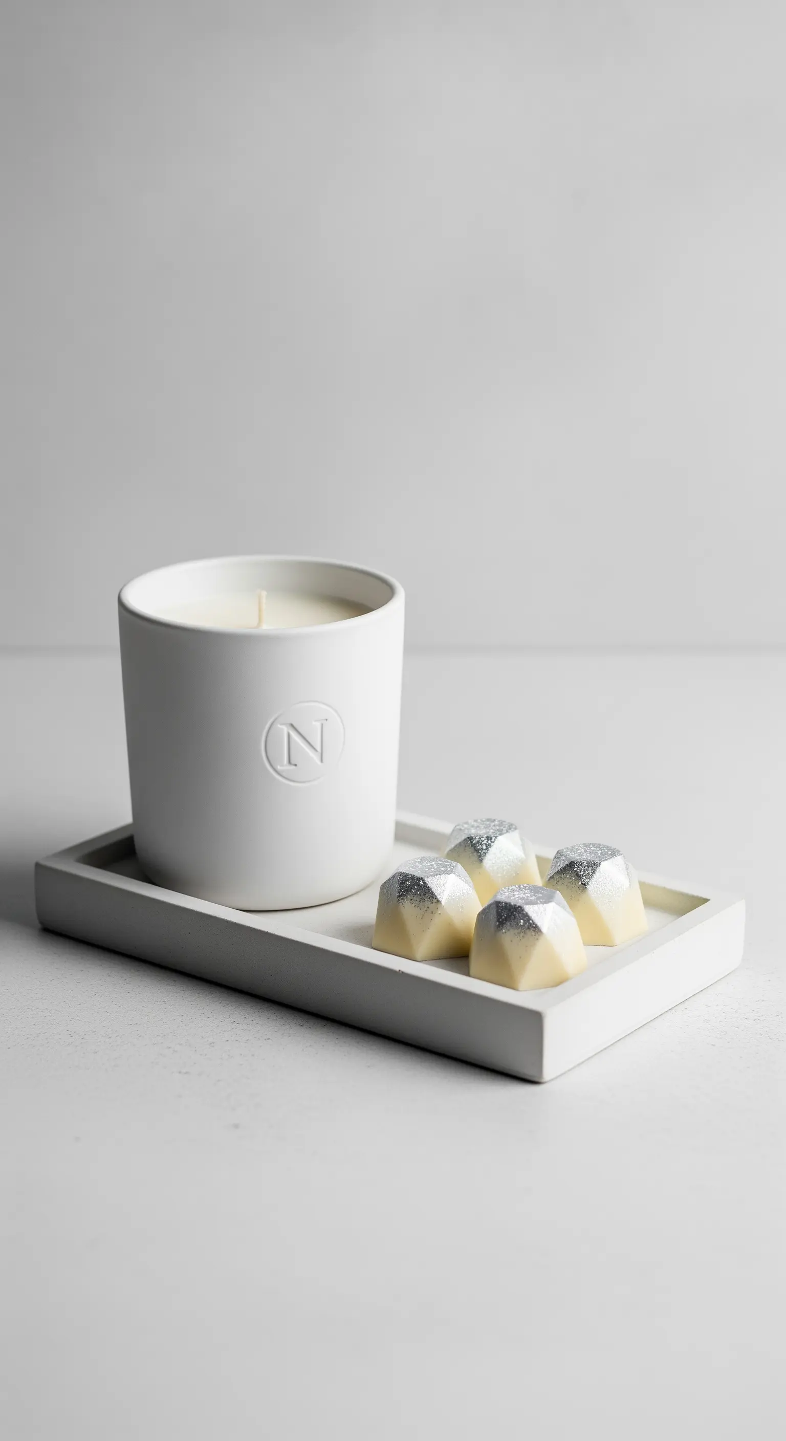 Candela bianca minimalista su vassoio in cemento con cioccolatini a forma di diamante.