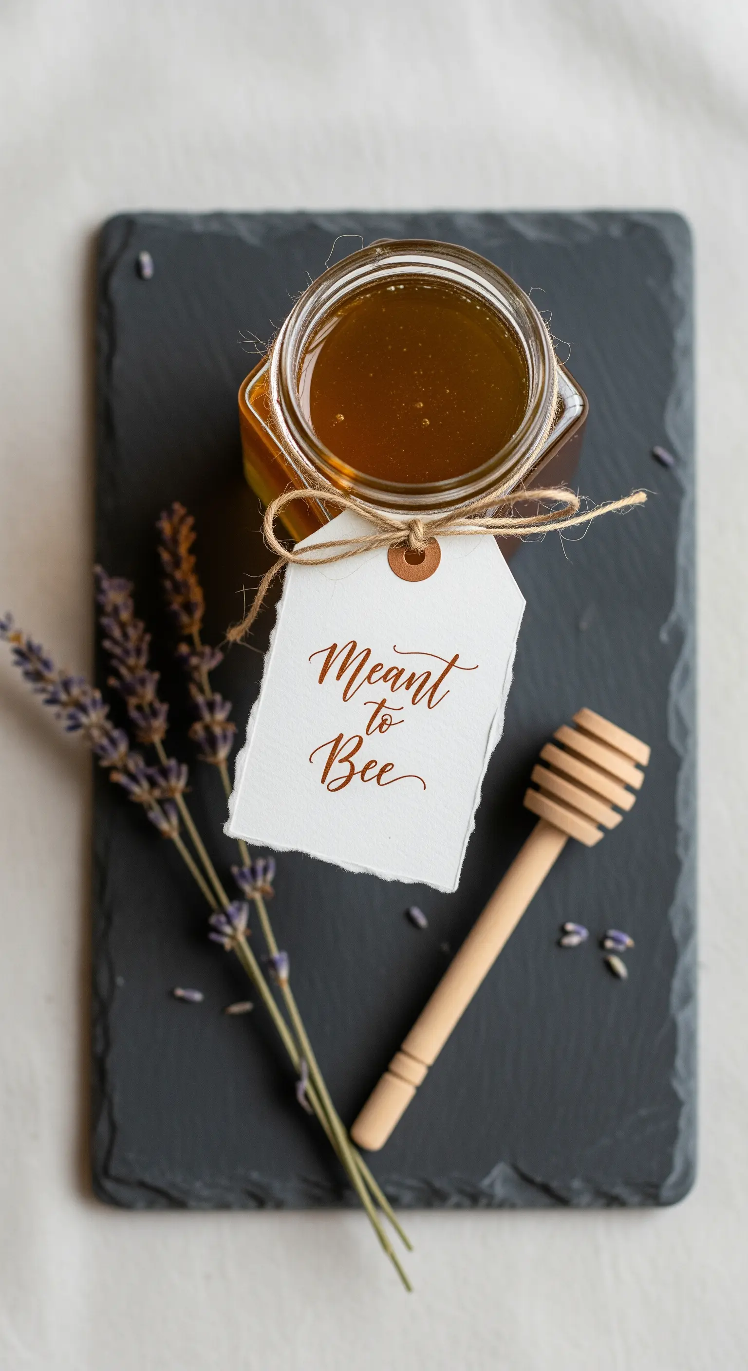 Vasetto di miele con etichetta calligrafata e lavanda secca su una base di ardesia.