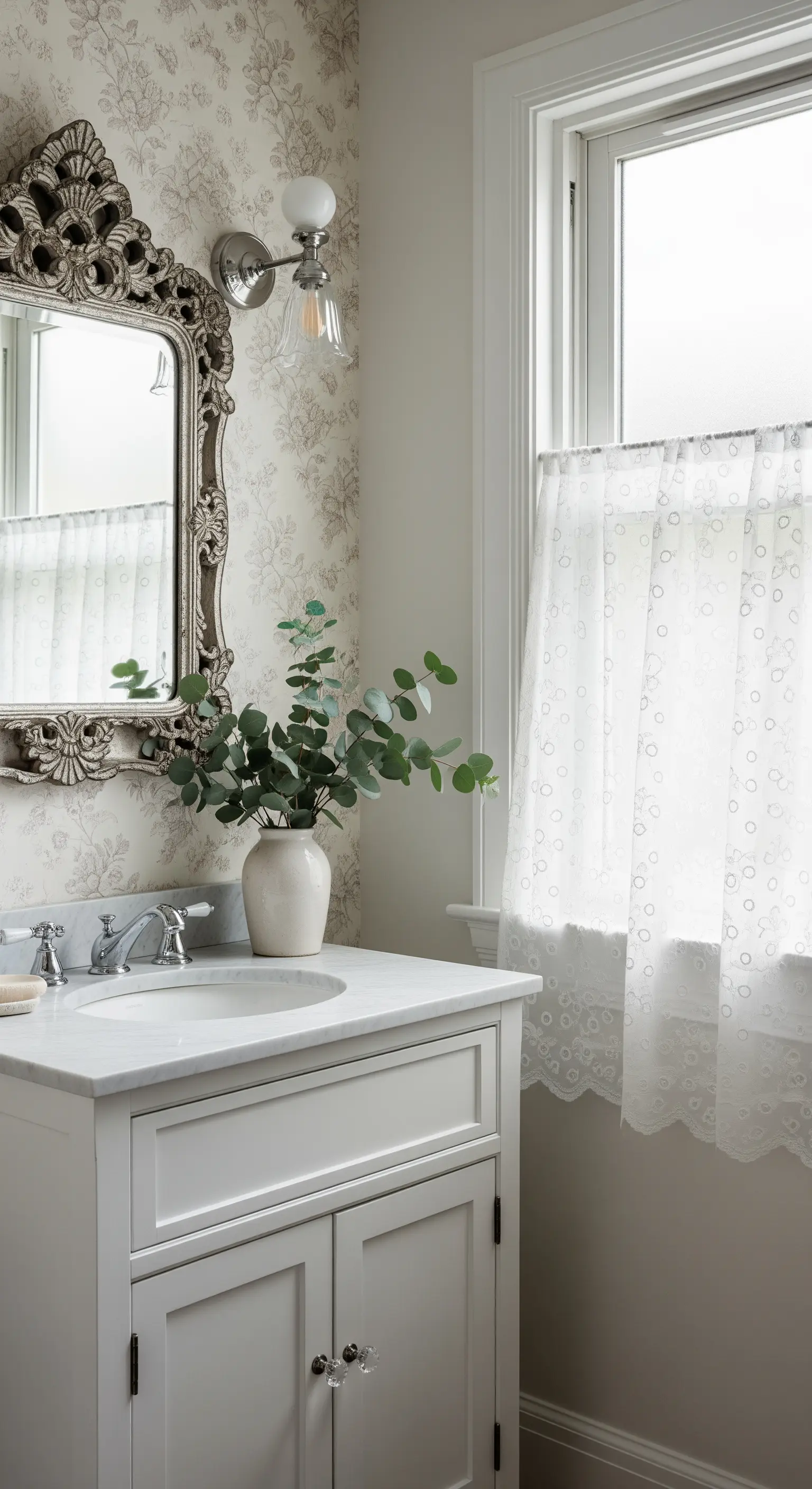 Bagno con mobile bianco, specchio argentato, carta da parati floreale e tende in pizzo.