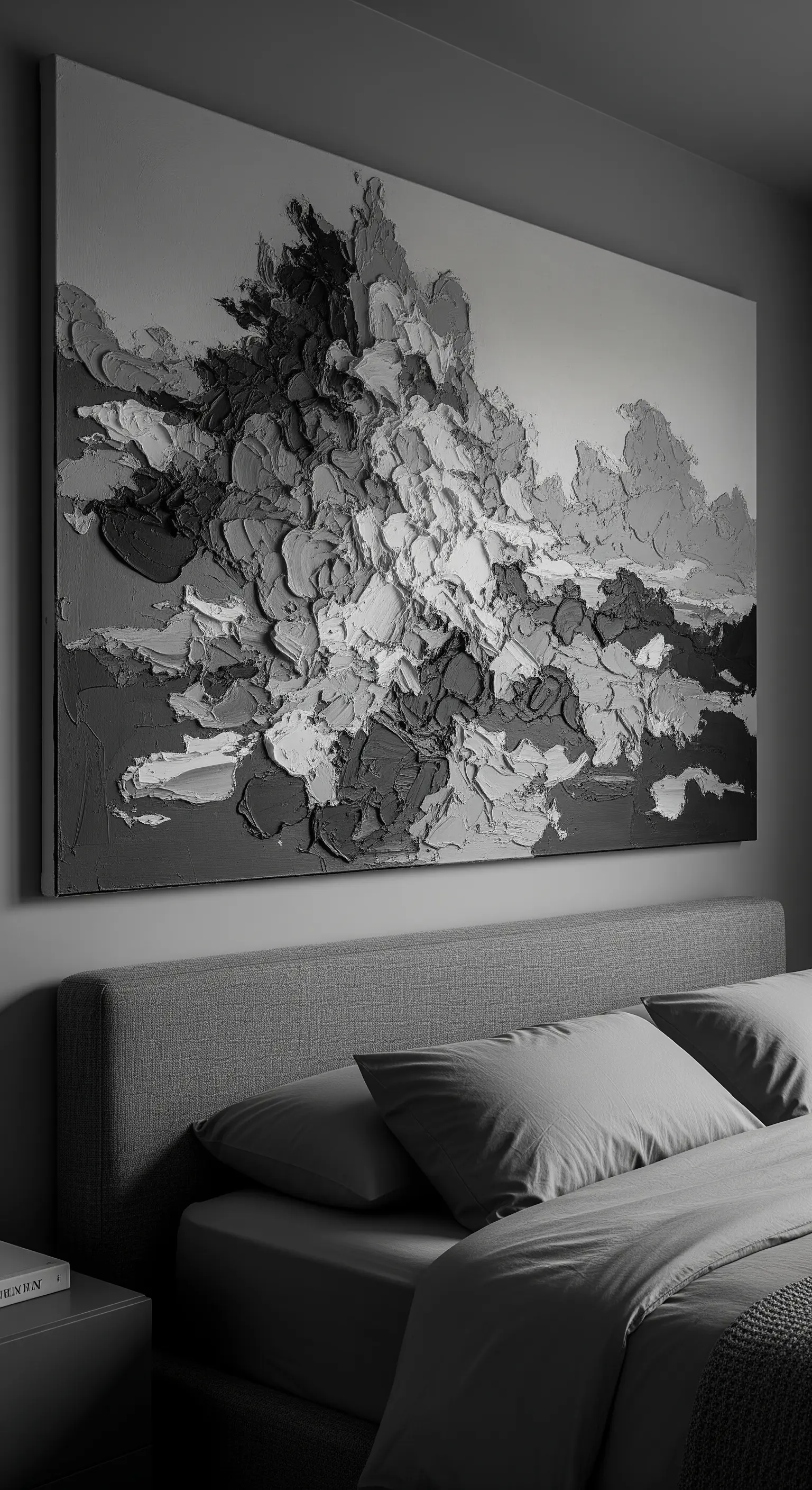 Grande quadro materico astratto in bianco, grigio e nero sopra un letto con testiera grigia.