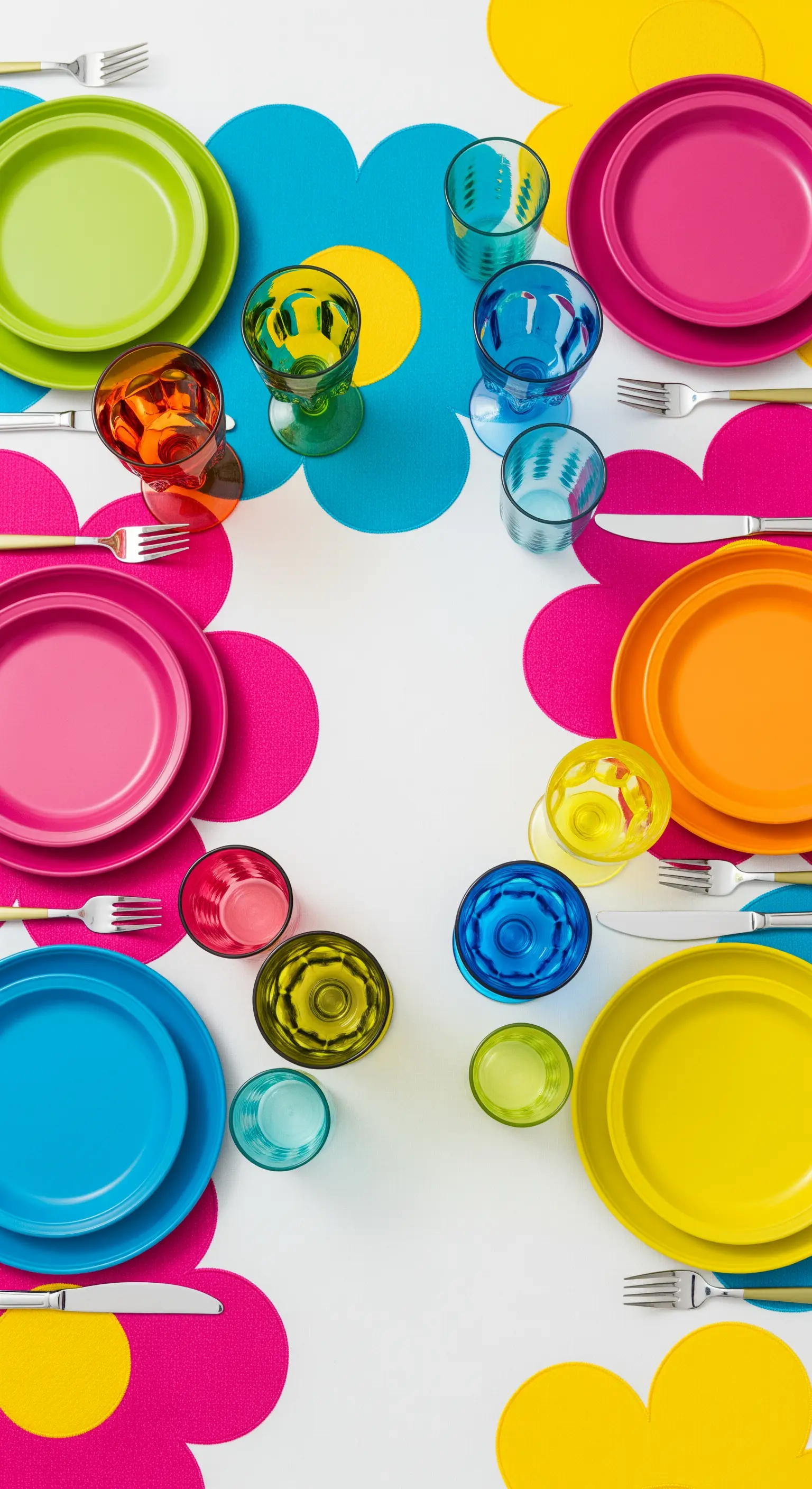 Tavola Pop Art con tovagliette a fiori stilizzati e piatti e bicchieri in colori primari.