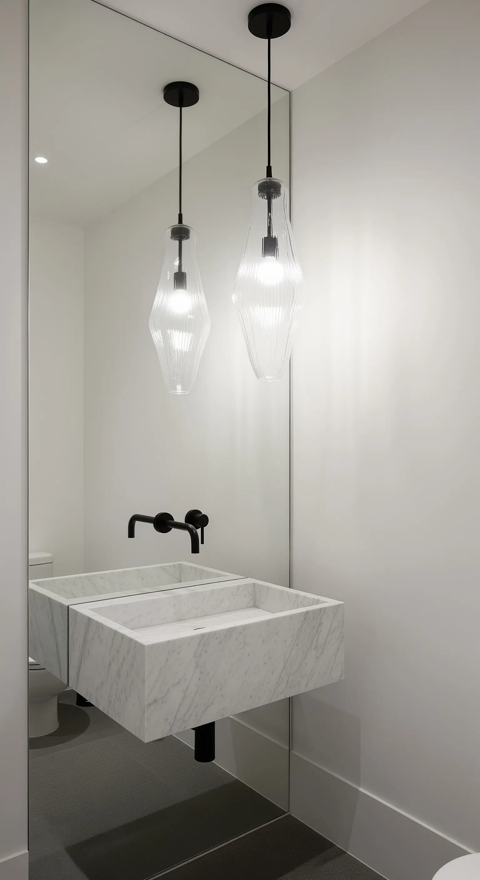Bagno minimalista con una parete a specchio a tutta altezza dietro un lavabo in marmo.