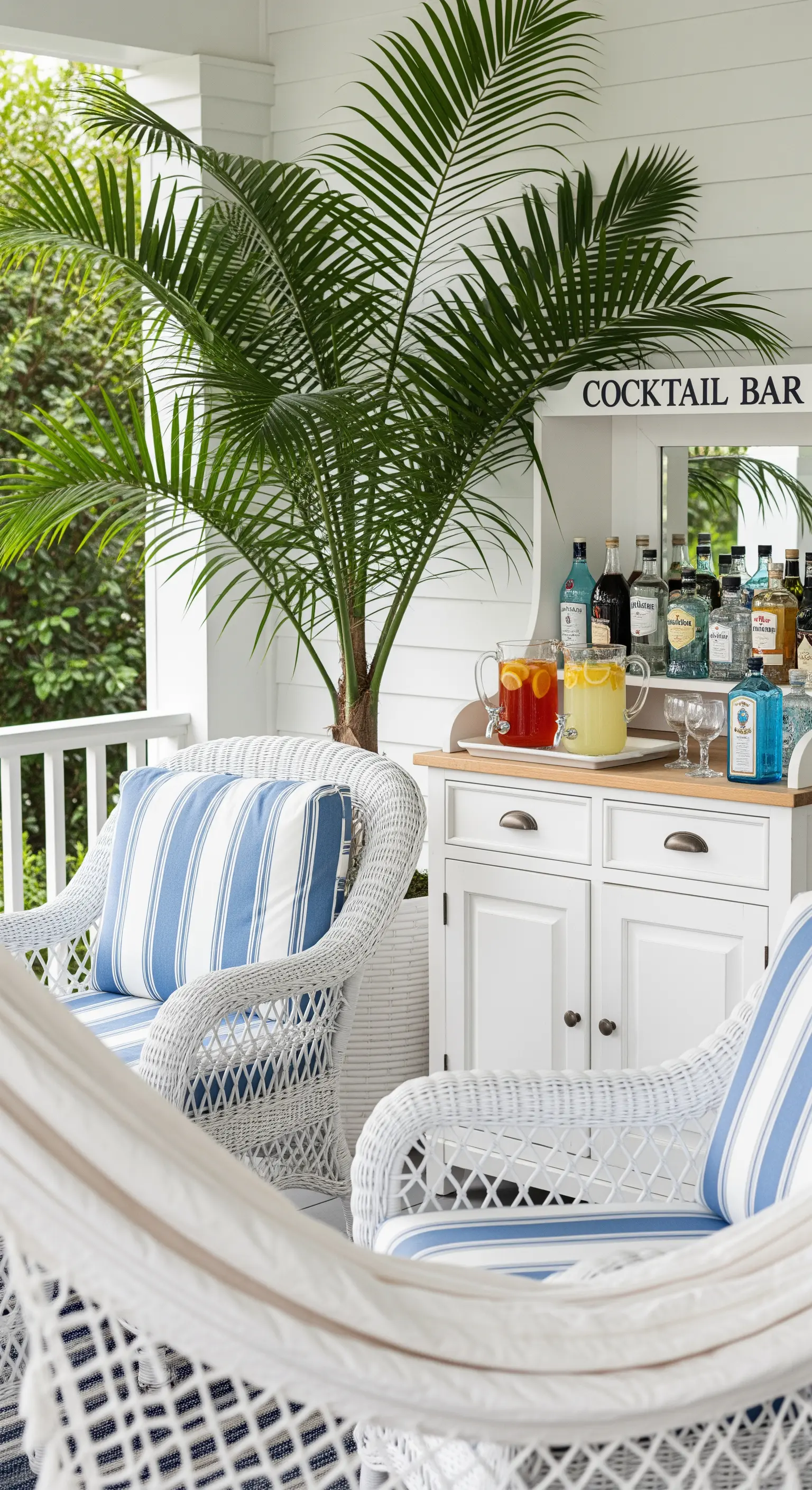 Portico bianco in stile Hamptons con poltrone in vimini, cuscini a righe blu e mobile bar