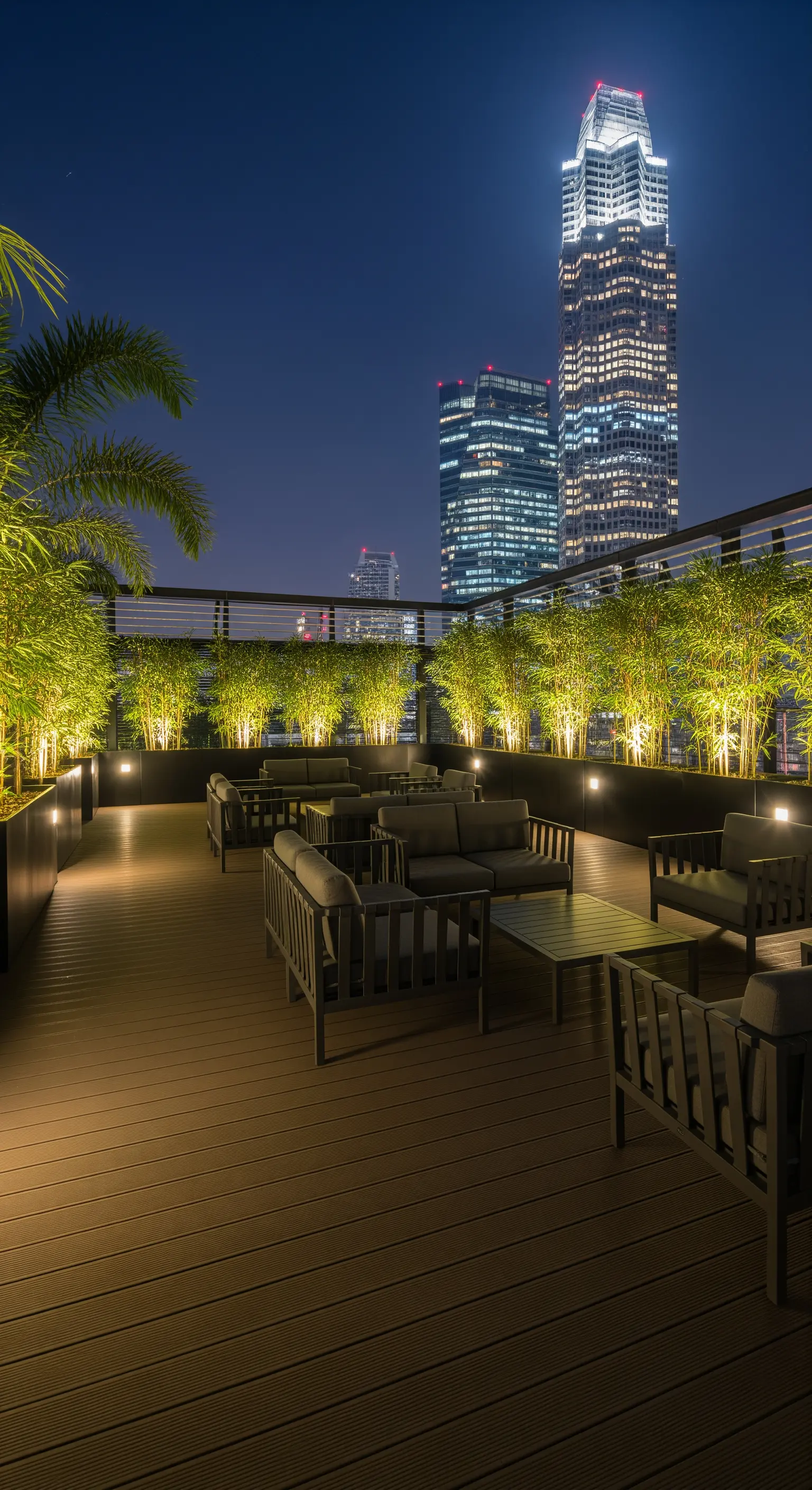 Terrazza panoramica di notte con divani scuri e una siepe di bambù illuminata dal basso.
