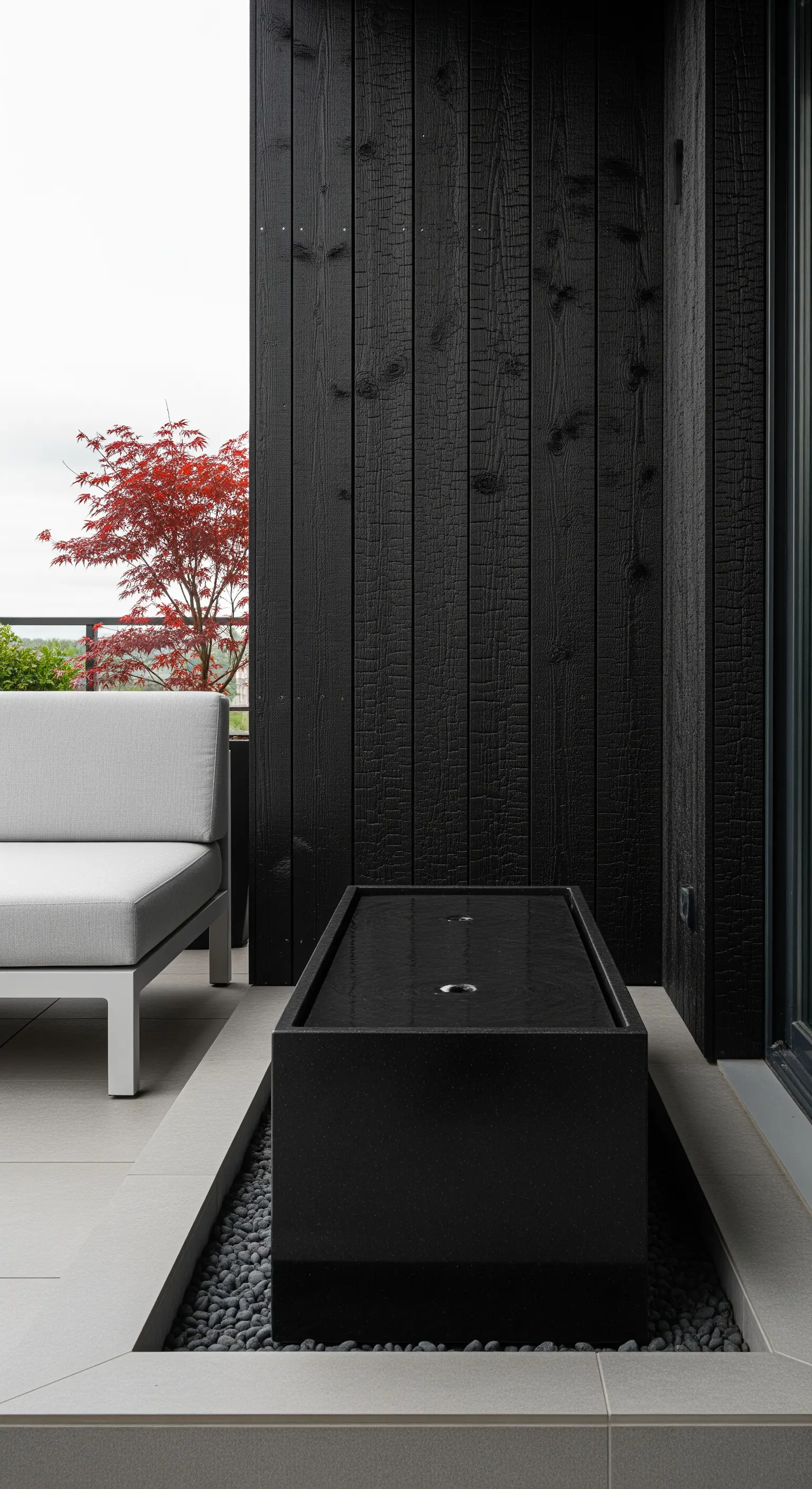 Balcone moderno con parete in legno nero bruciato e fontana rettangolare in granito.