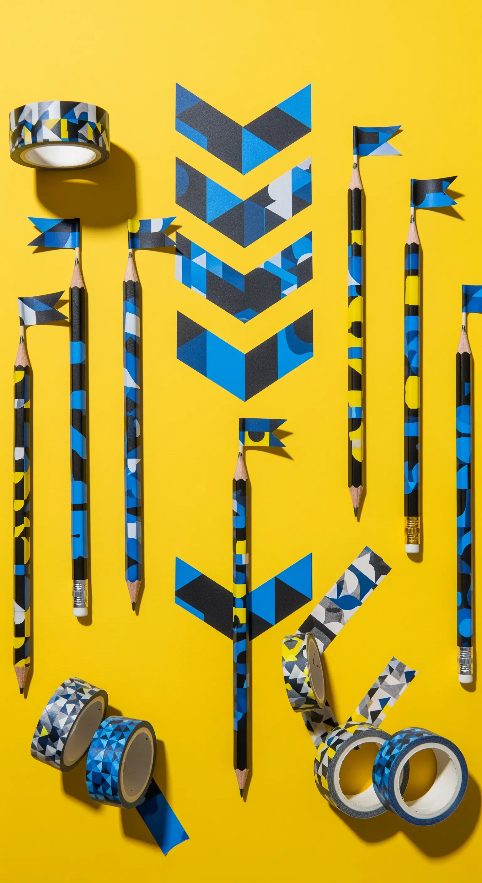Matite decorate con washi tape a motivi geometrici blu, neri e bianchi su fondo giallo.