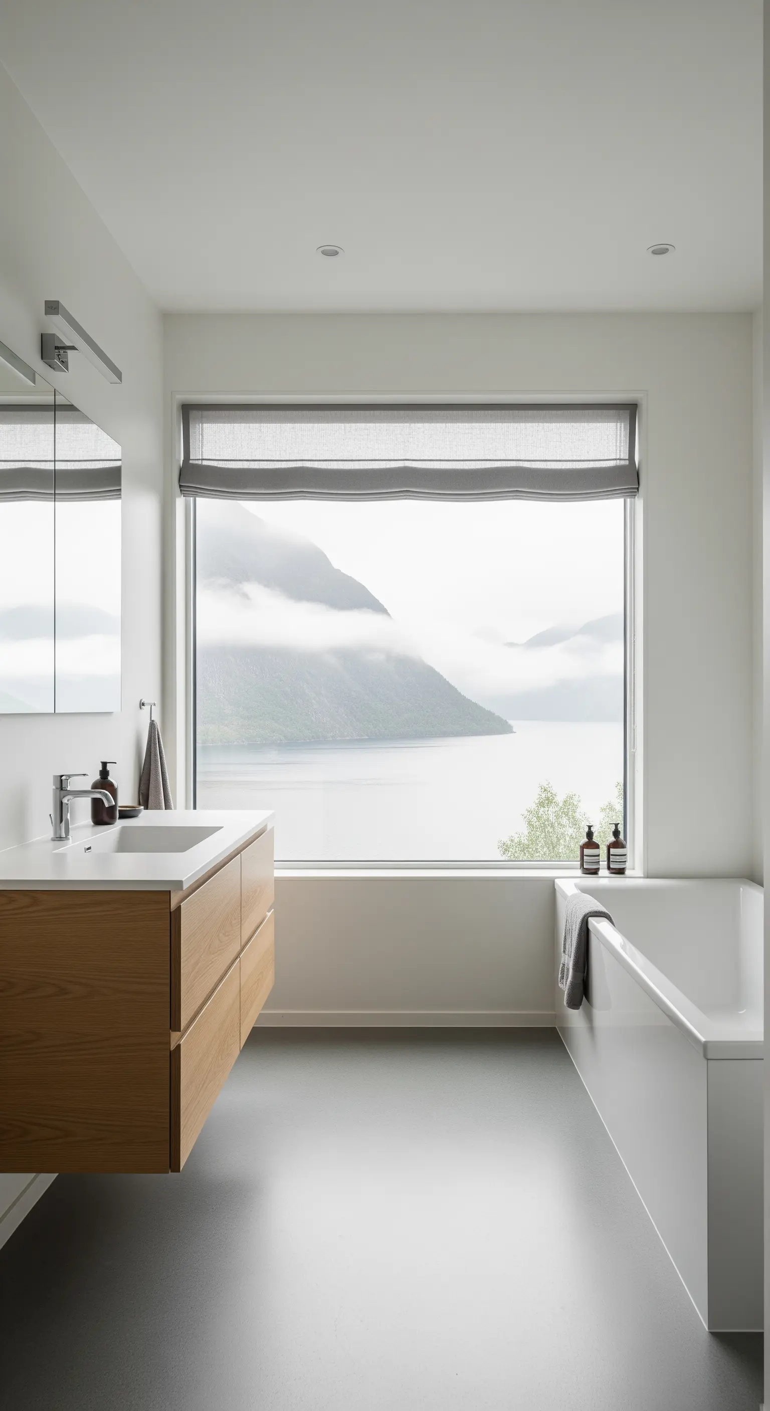Bagno minimalista con lavabo sospeso in legno e grande finestra con vista su un fiordo nebbioso.