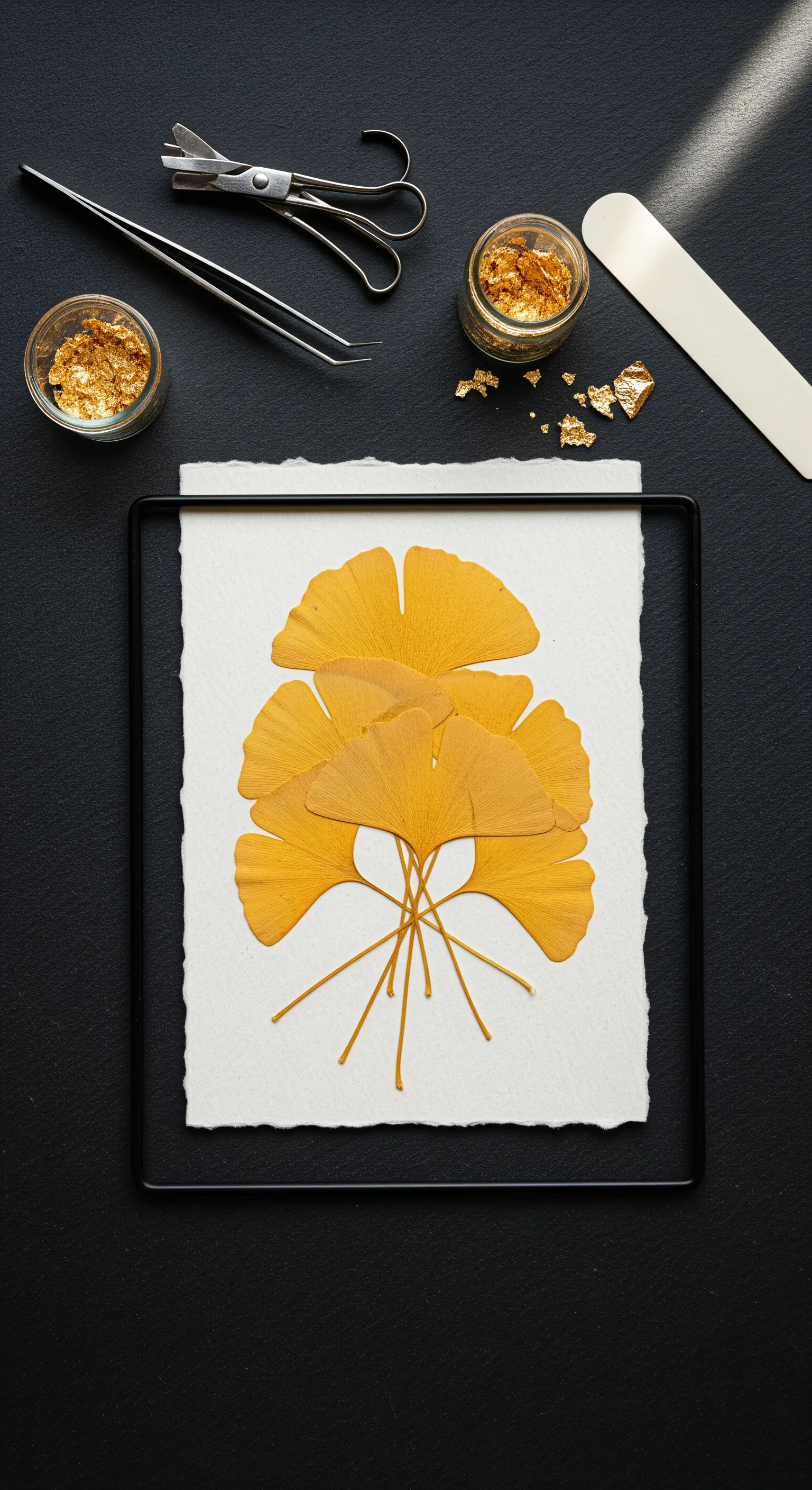 Foglie di ginkgo pressate e scaglie di foglia d'oro su un tavolo da lavoro nero.