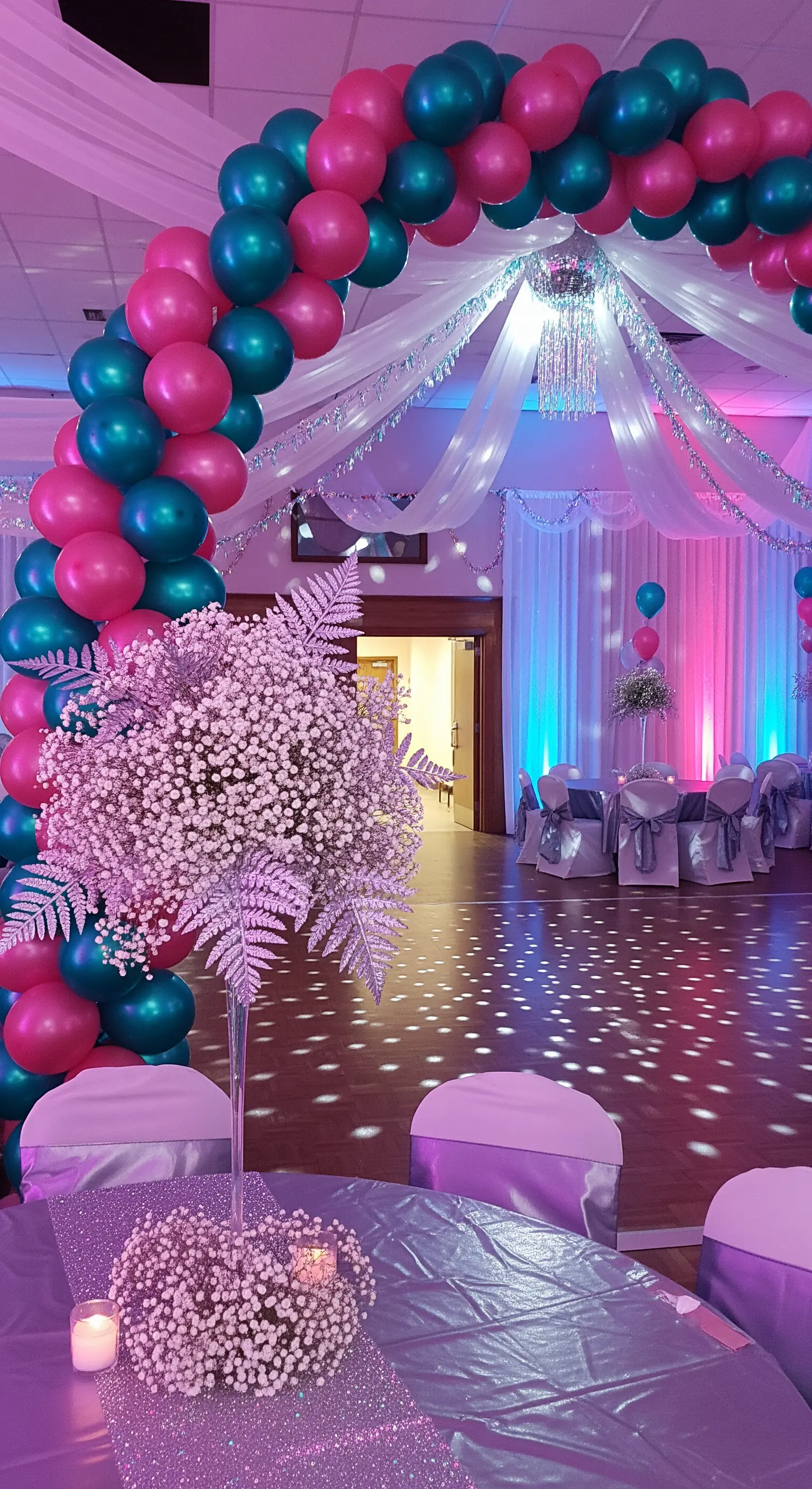 Sala da ballo decorata per una festa anni '80 con palloncini magenta e teal, e luci viola.