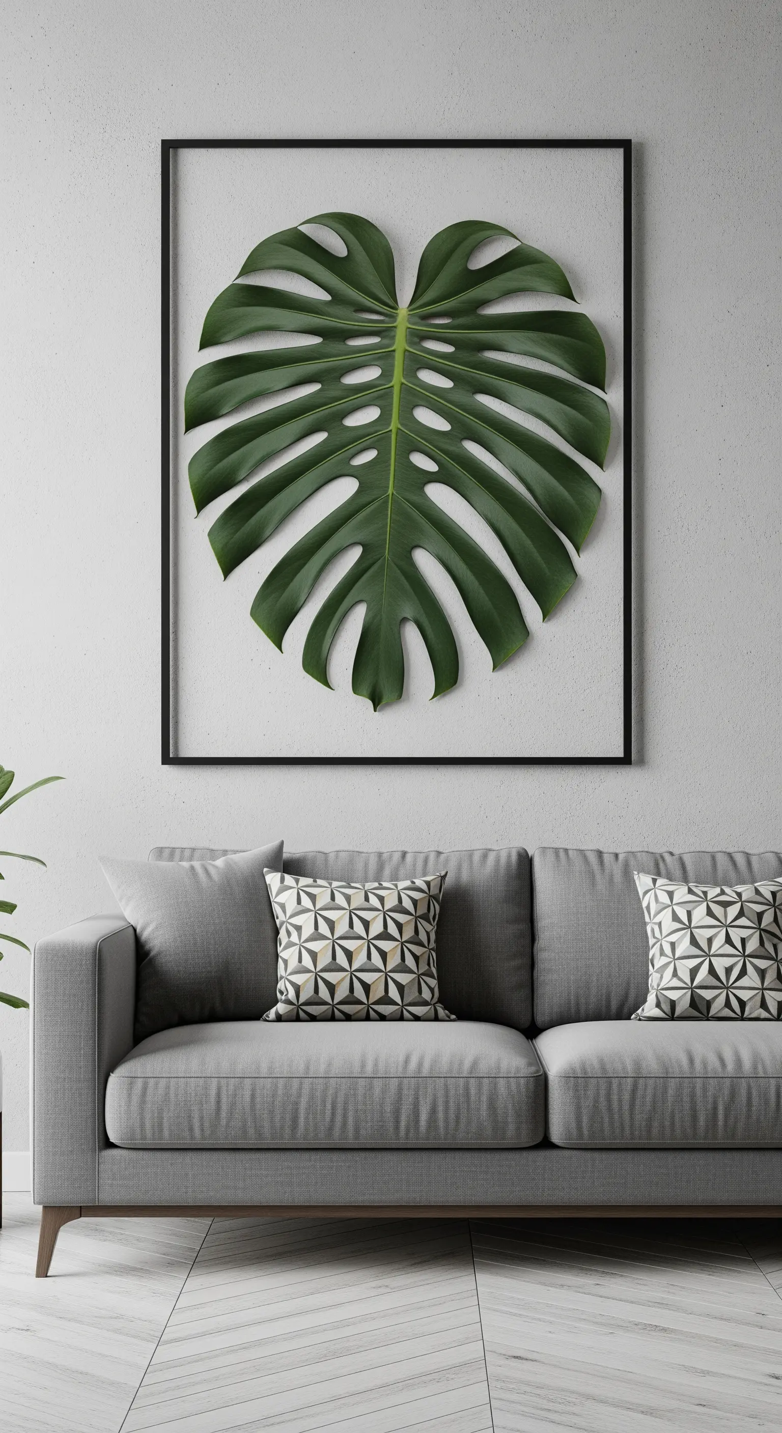 Gigantesca foglia di Monstera incorniciata senza vetro sopra un divano grigio.