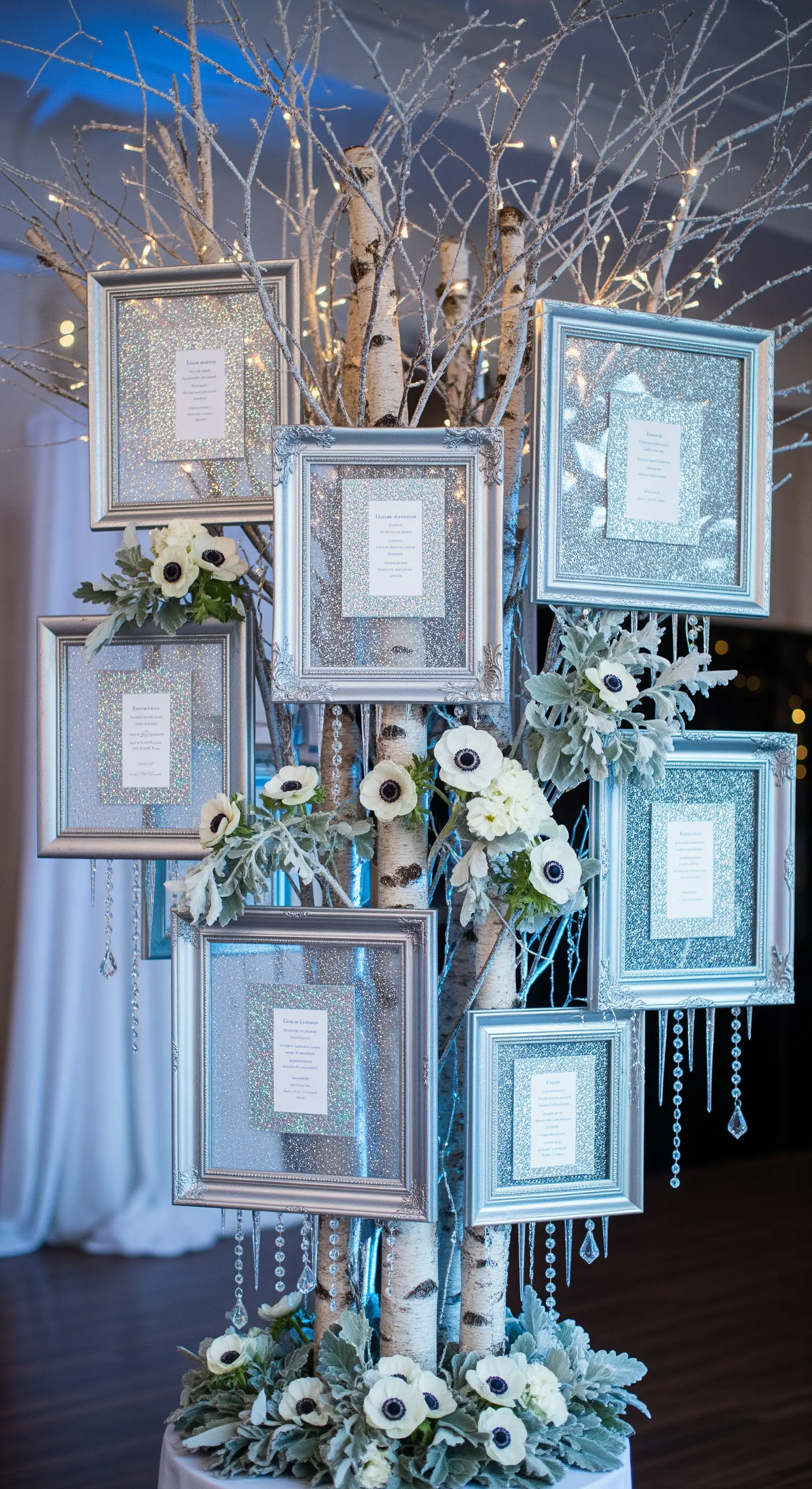 Tableau mariage invernale con cornici argentate glitterate su tronchi di betulla e fiori bianchi.