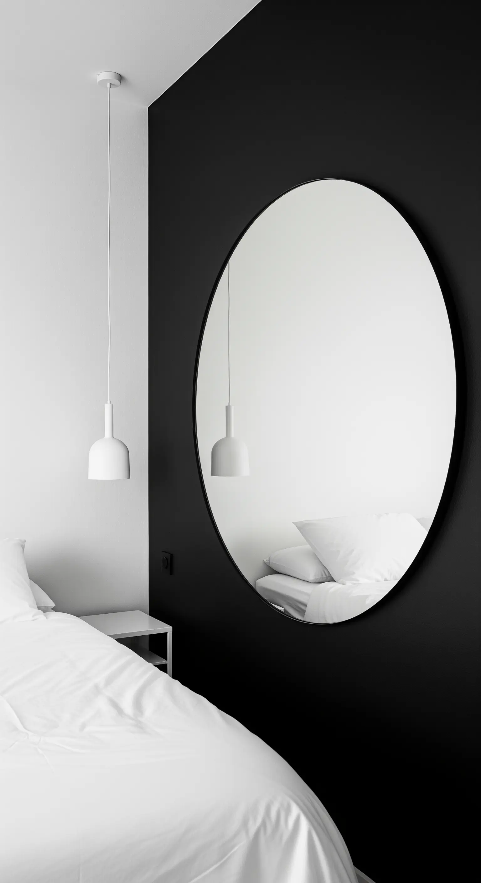 Grande specchio rotondo con cornice nera appeso su una parete nera in una camera da letto minimalista.