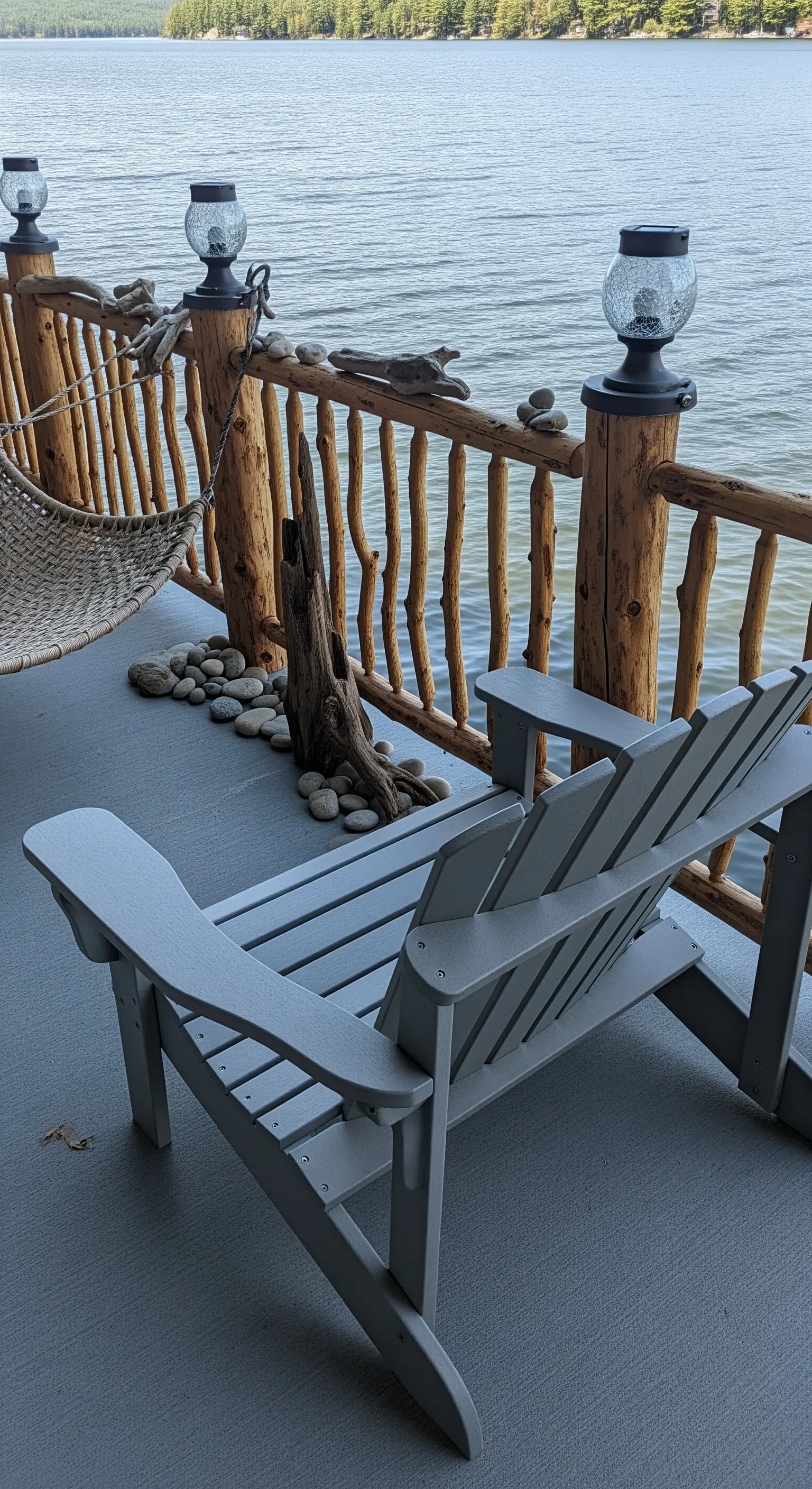 Terrazzo sul lago con sedie Adirondack grigie e ringhiera in tronchi di legno grezzo.