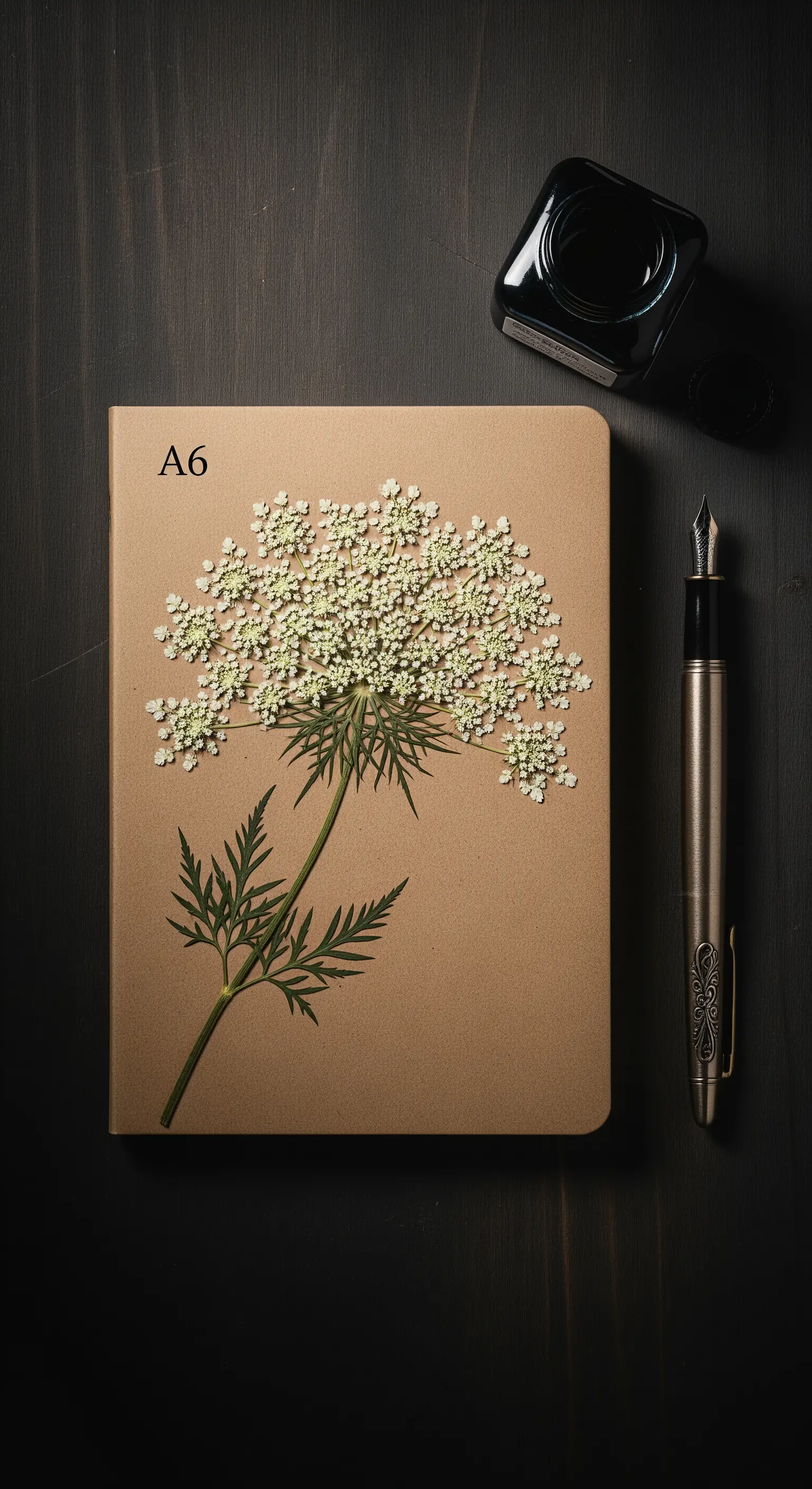 Taccuino con copertina in carta kraft e un fiore di carota selvatica pressato al centro.