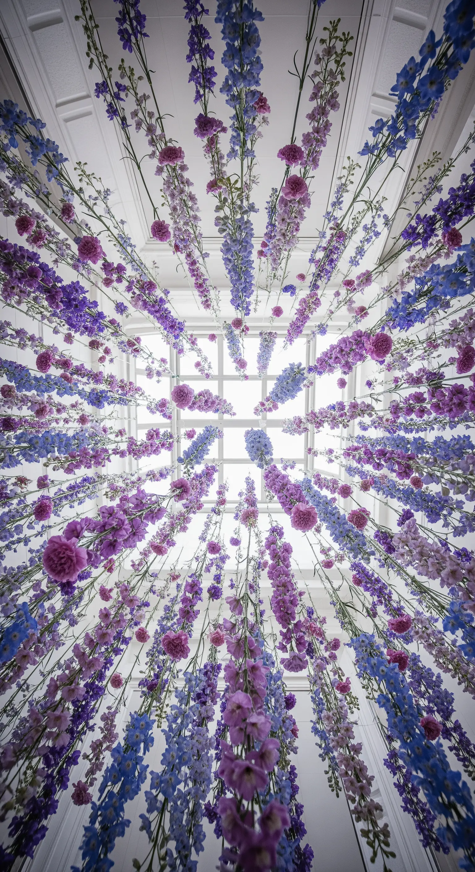 Installazione di fiori viola, blu e rosa che pendono dal soffitto, vista dal basso.