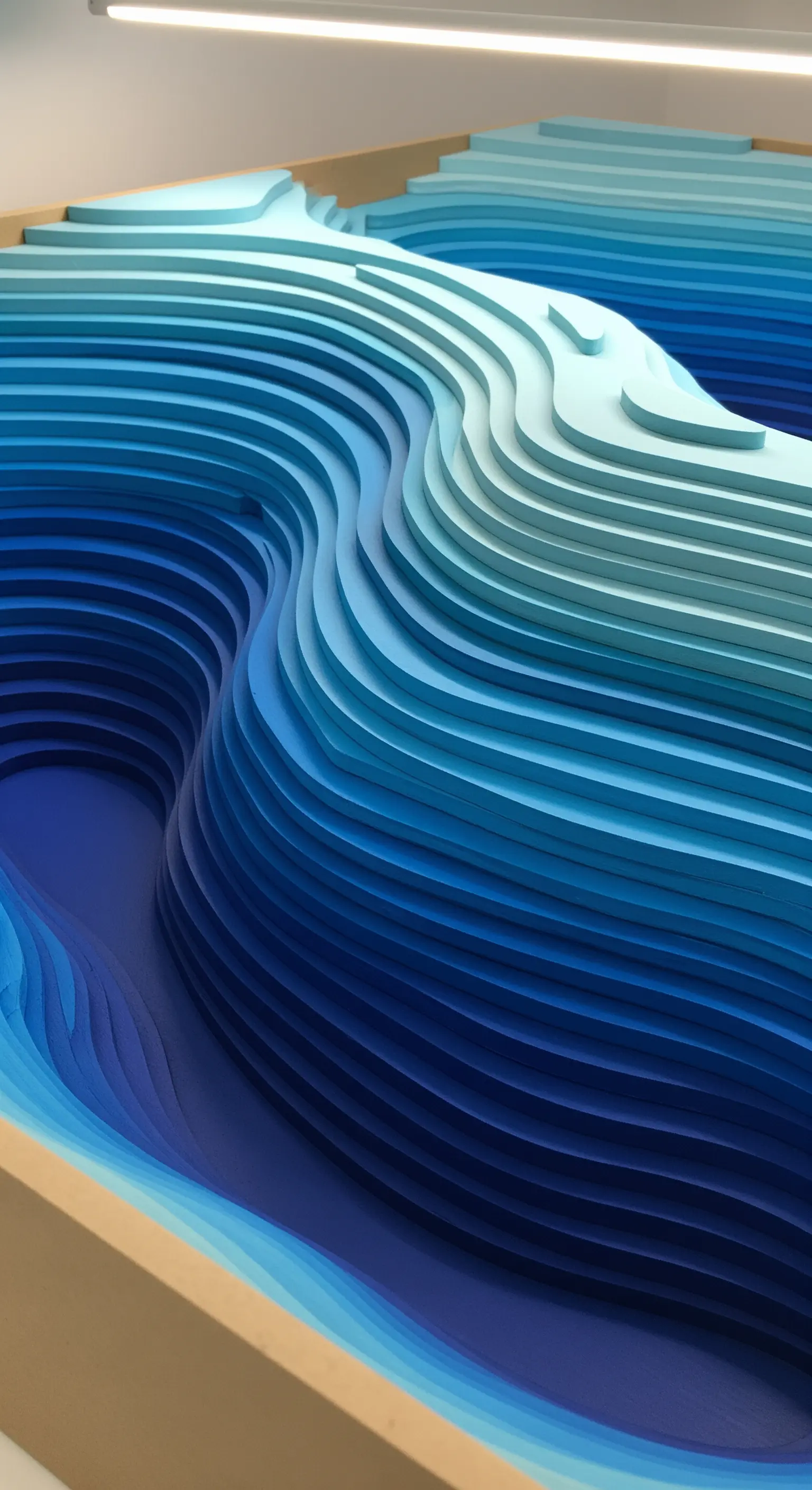 Modello topografico tridimensionale realizzato con strati di carta sovrapposti in diverse tonalità di blu.