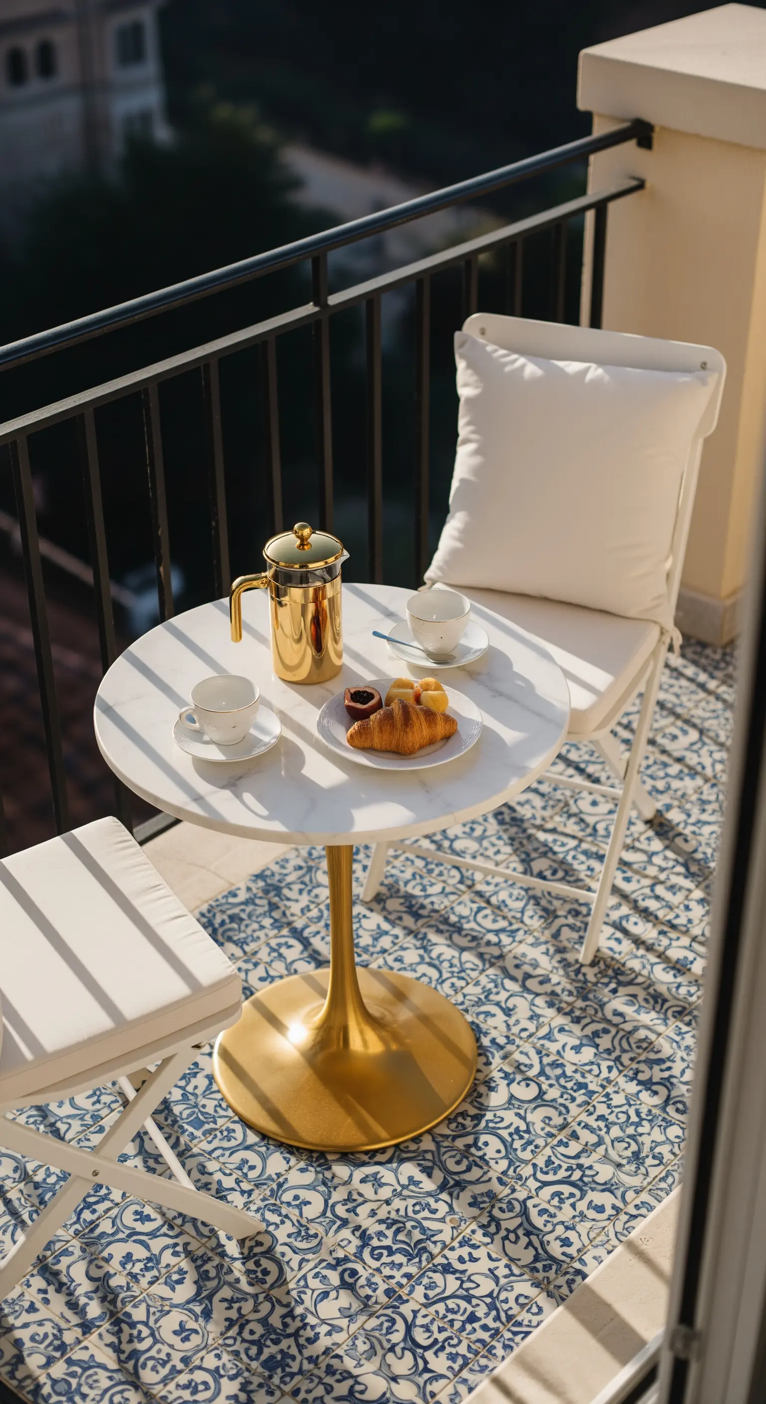 Piccolo balcone con tavolino in marmo e base dorata, sedie bianche e tappeto a maioliche.