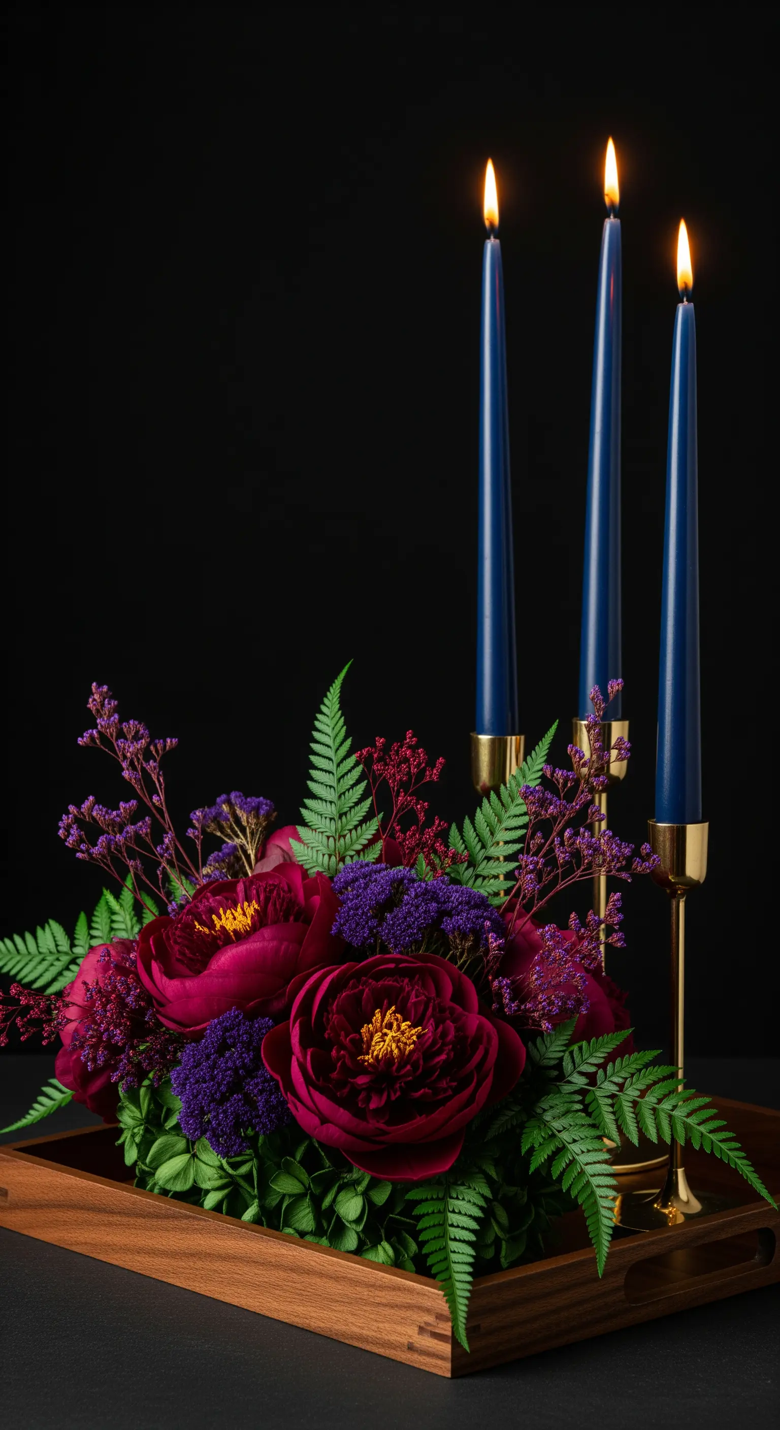 Composizione drammatica con candele blu, peonie magenta e felci su sfondo nero.