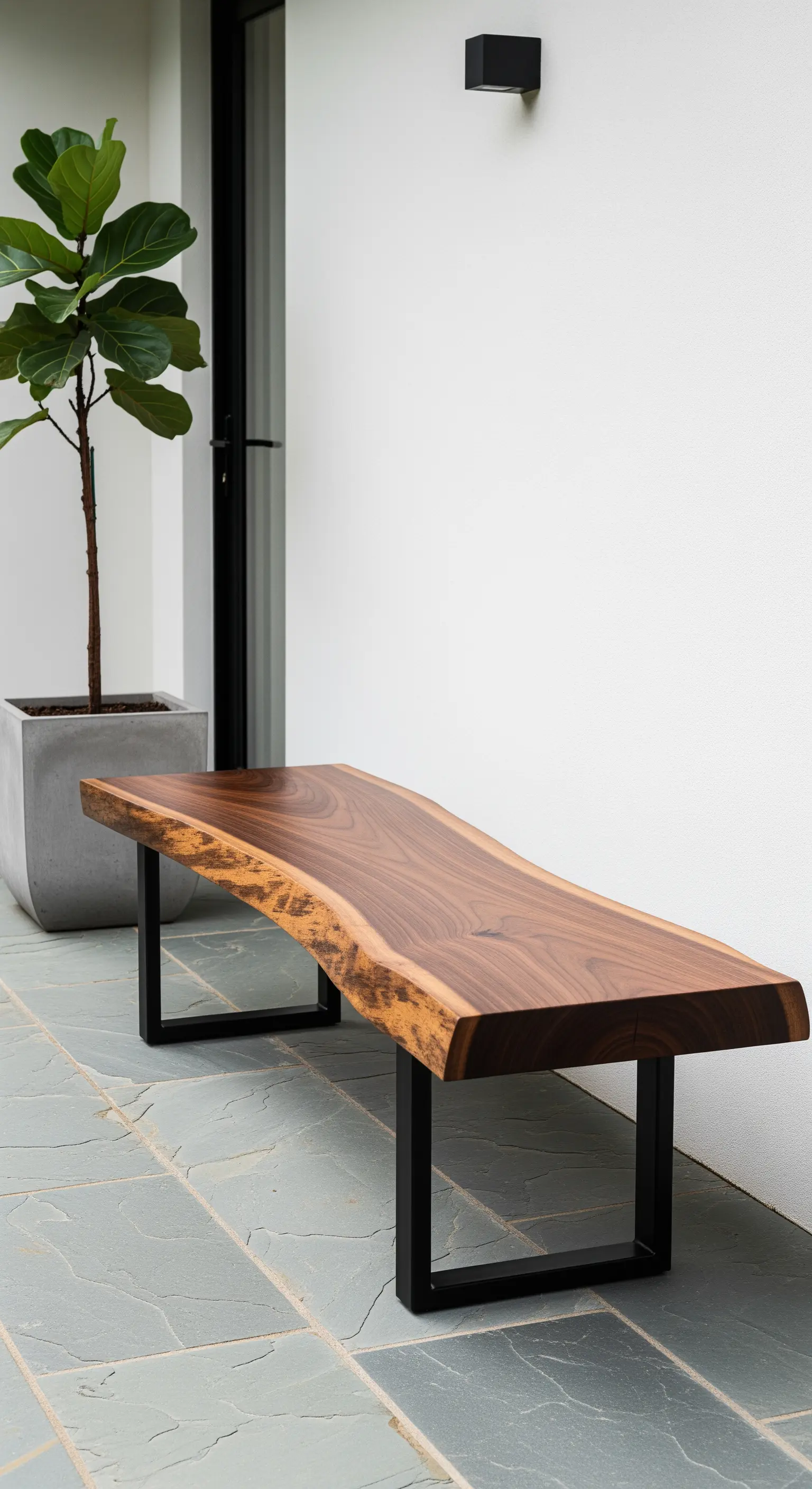 Panca moderna con piano in legno massiccio scuro e gambe in metallo nero, su un patio di ardesia.