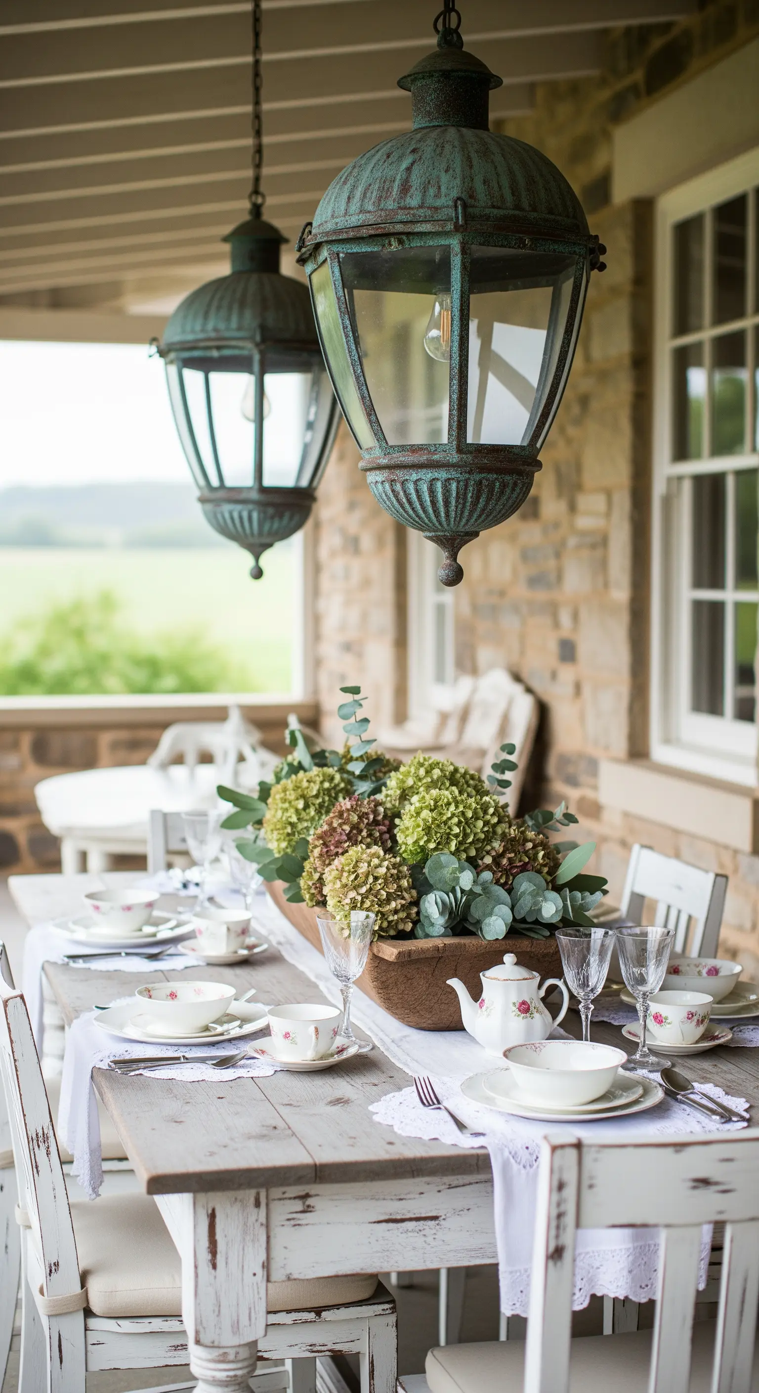 Tavola da pranzo in veranda con sedie bianche, lanterne vintage e ortensie secche.