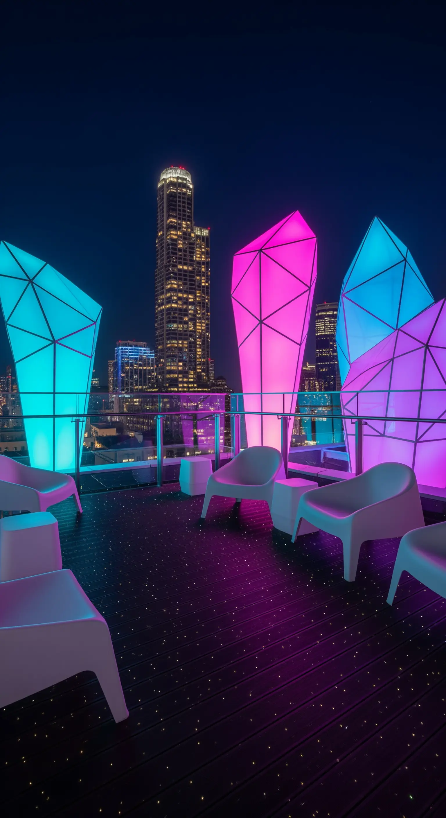 Terrazza con grandi sculture geometriche illuminate di blu e rosa e vista sulla città.