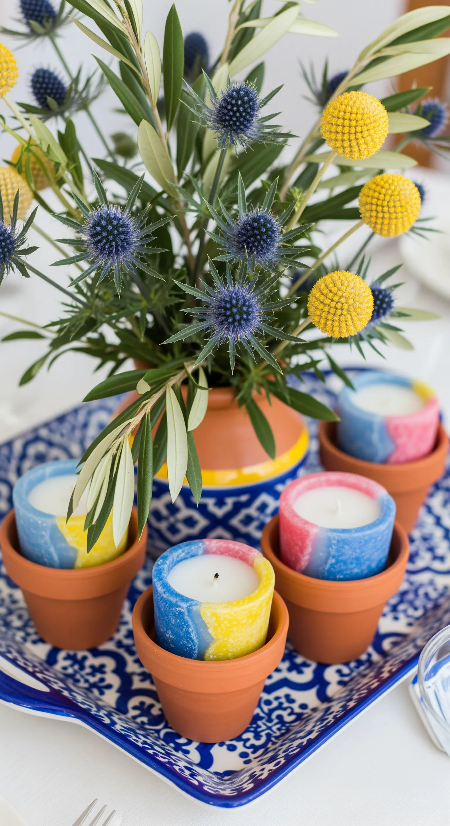 Centrotavola in stile mediterraneo con candele in vasetti di terracotta e cardi blu.