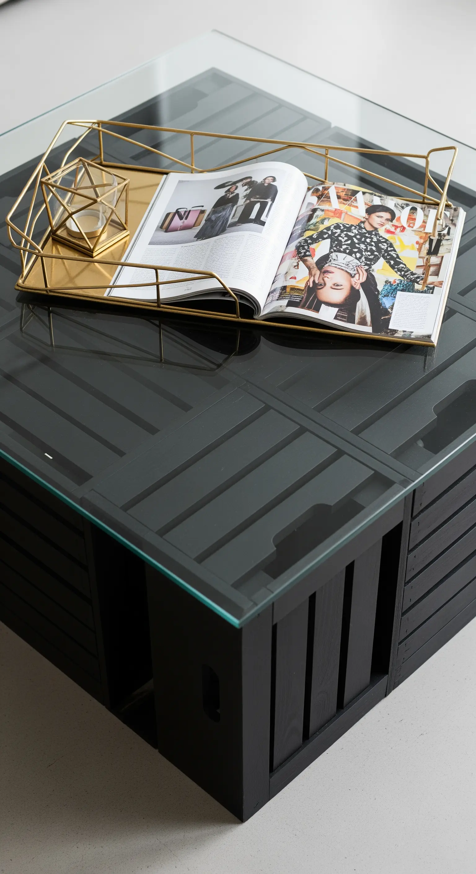 Tavolino quadrato nero composto da quattro cassette di legno e un piano in vetro trasparente.