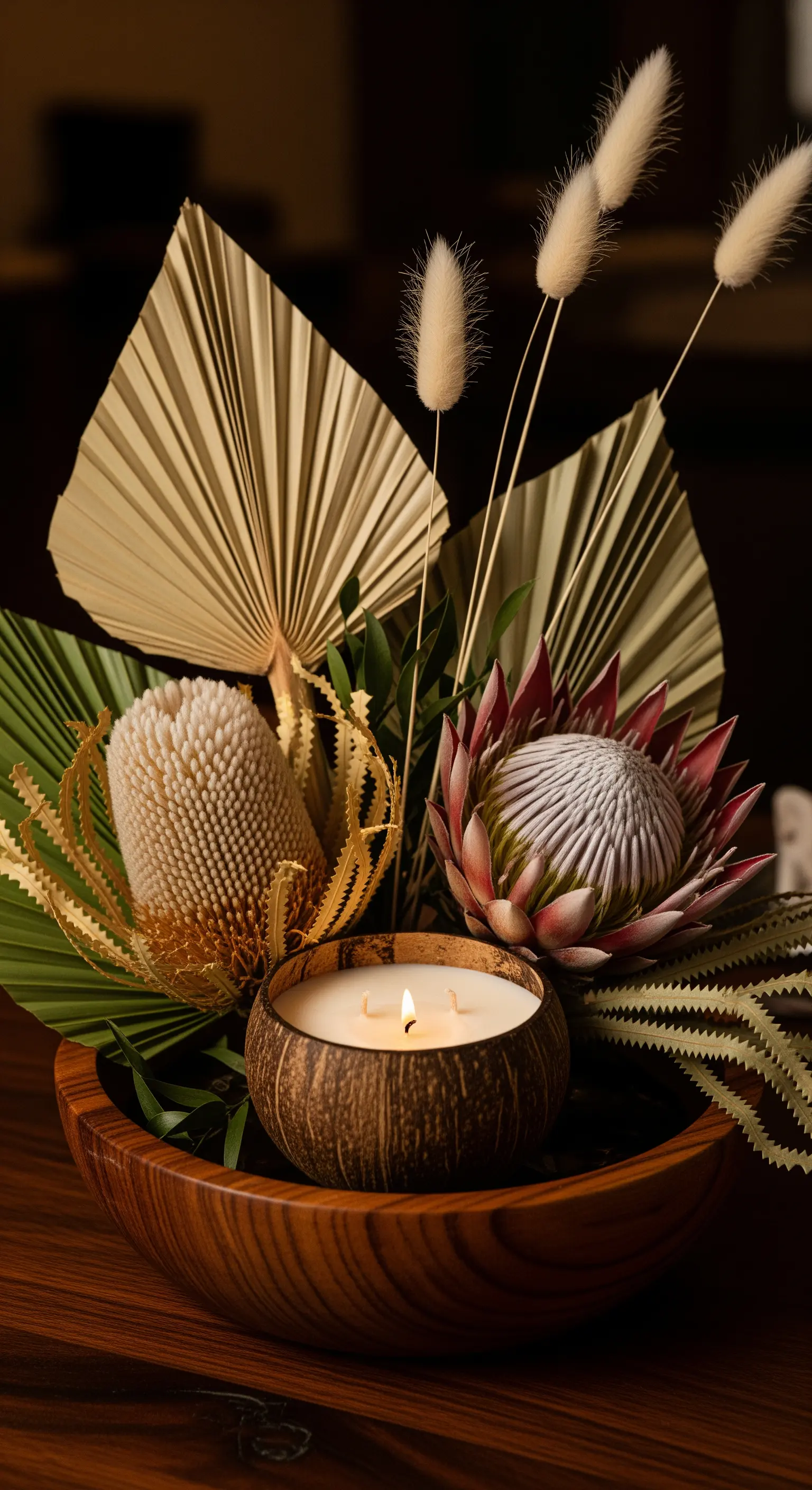 Composizione tropicale con candela in noce di cocco, protea e foglie di palma in una ciotola di legno.
