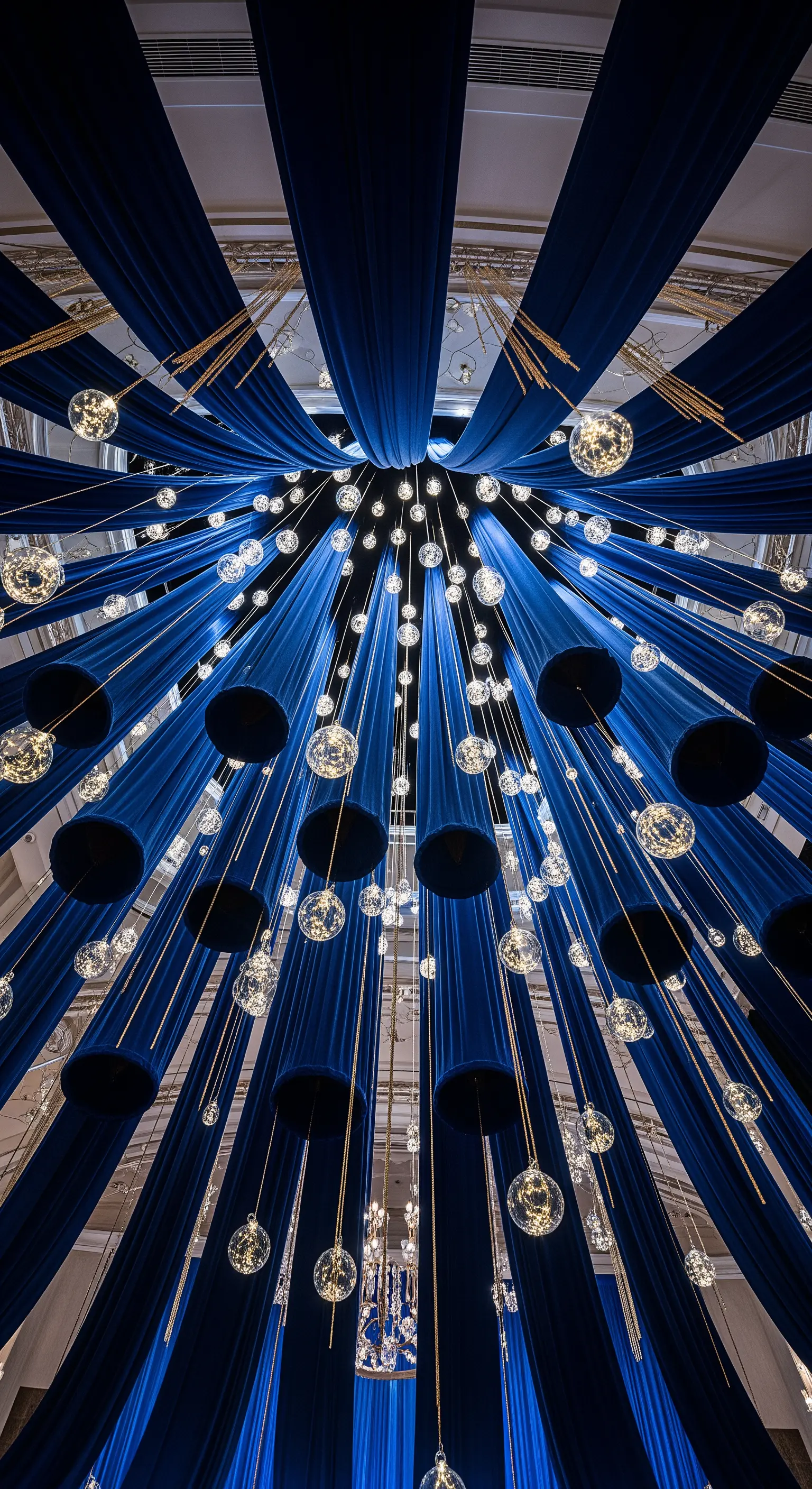 Installazione a soffitto con drappeggi in velluto blu e sfere di cristallo luminose pendenti.