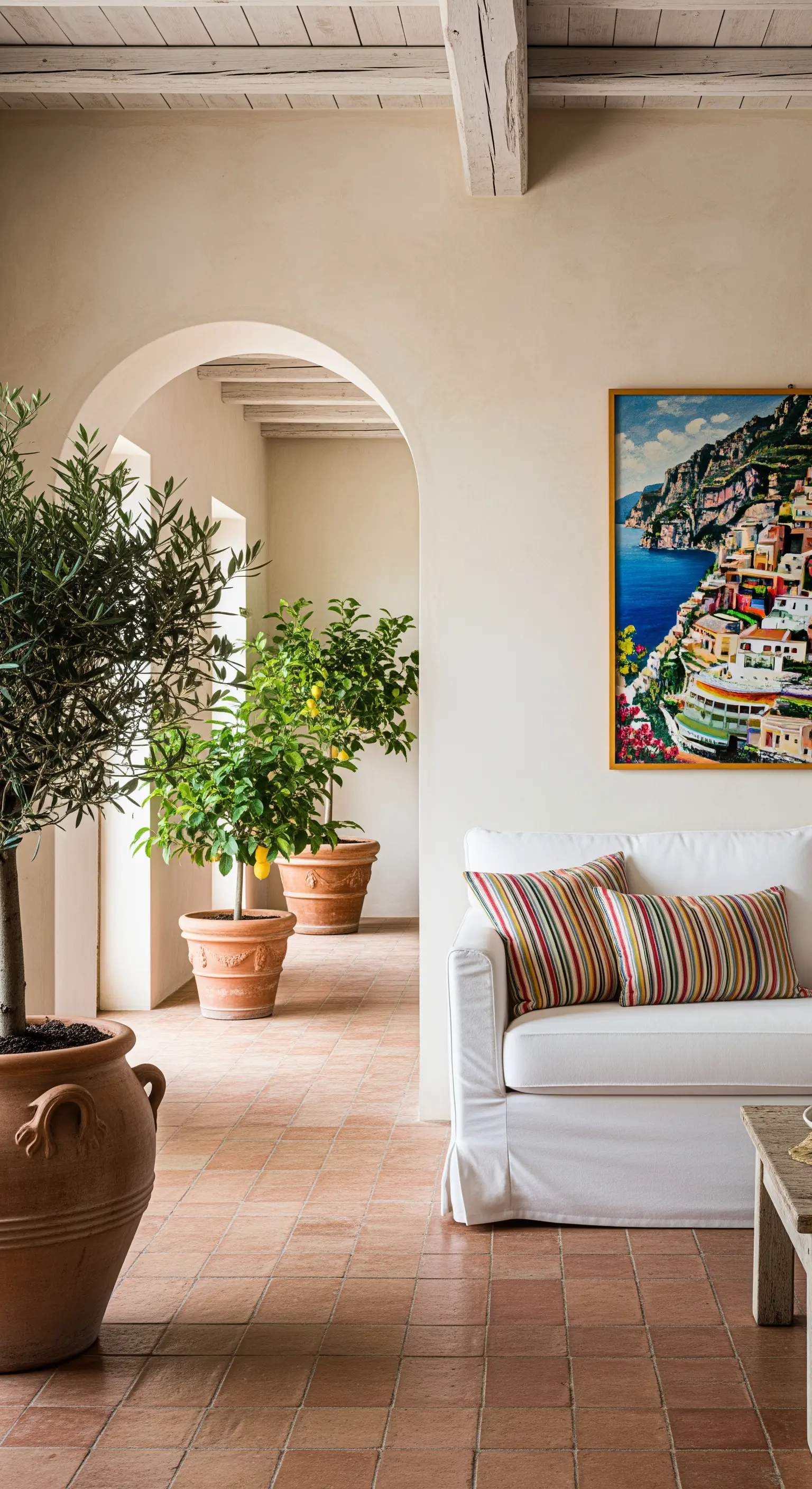 Interno in stile mediterraneo con divano bianco, pavimento in cotto e piante di limoni e ulivi.
