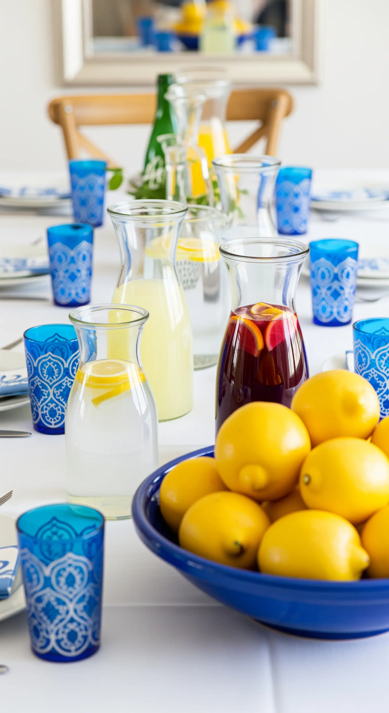 Tavola con caraffe di limonate e sangria, bicchieri blu e una ciotola di limoni.