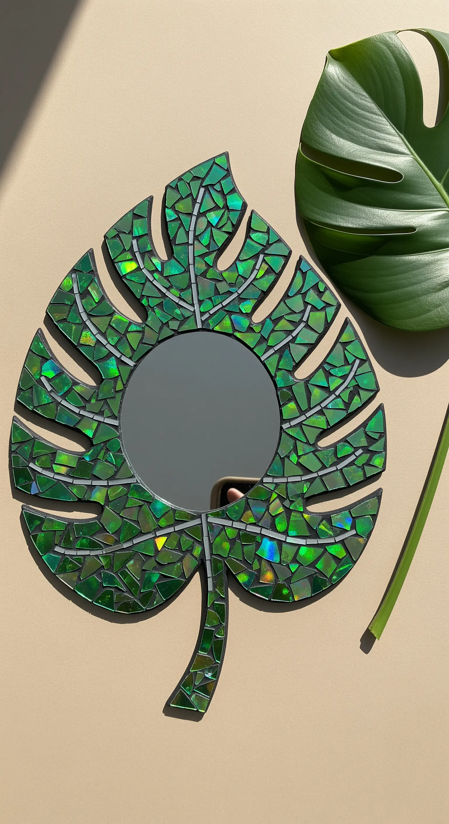 Specchio a forma di foglia di Monstera con mosaico di CD dipinti di verde.