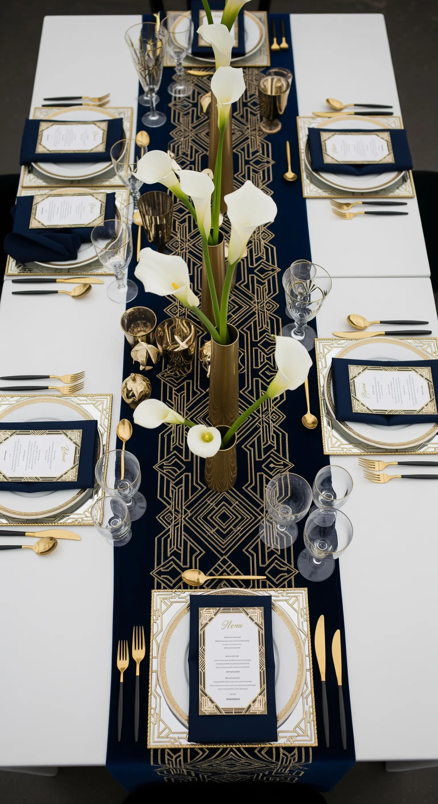 Tavola moderna con runner geometrico blu e oro, e calle bianche in un vaso dorato.