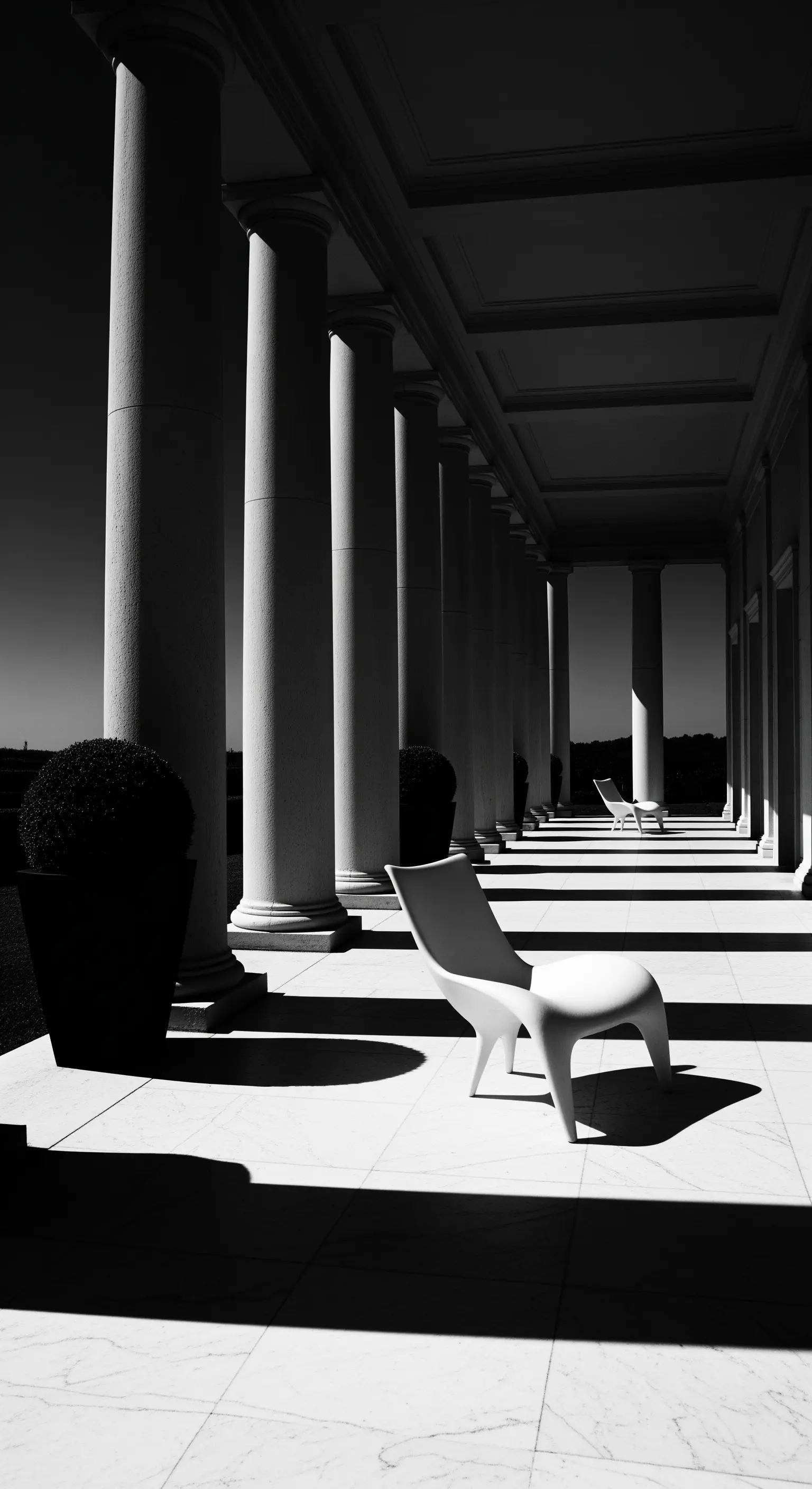Foto in bianco e nero di un portico con colonne che proiettano lunghe ombre su una sedia moderna