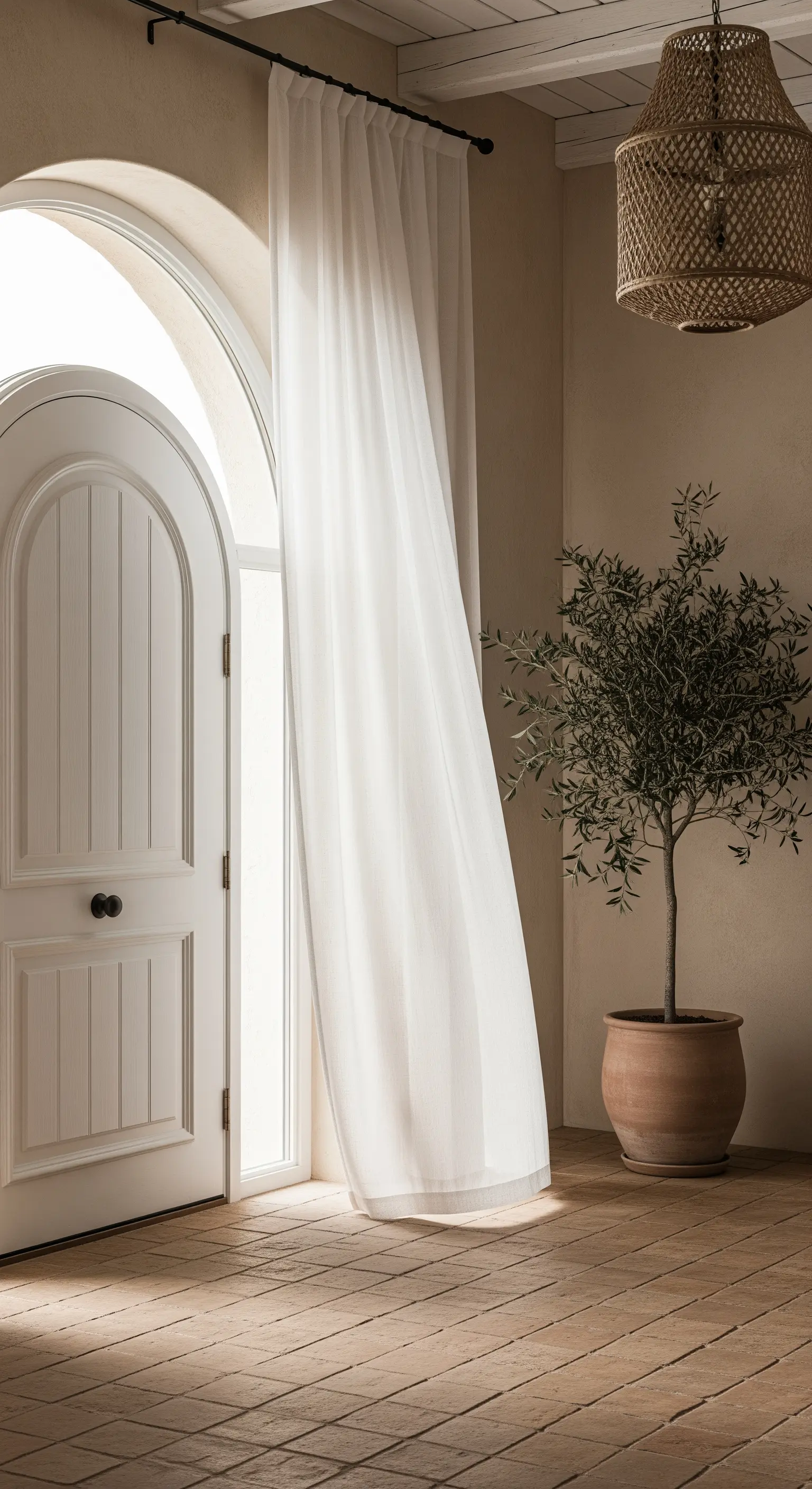 Porta ad arco bianca con una singola tenda in lino, pavimento in terracotta e un ulivo in vaso.
