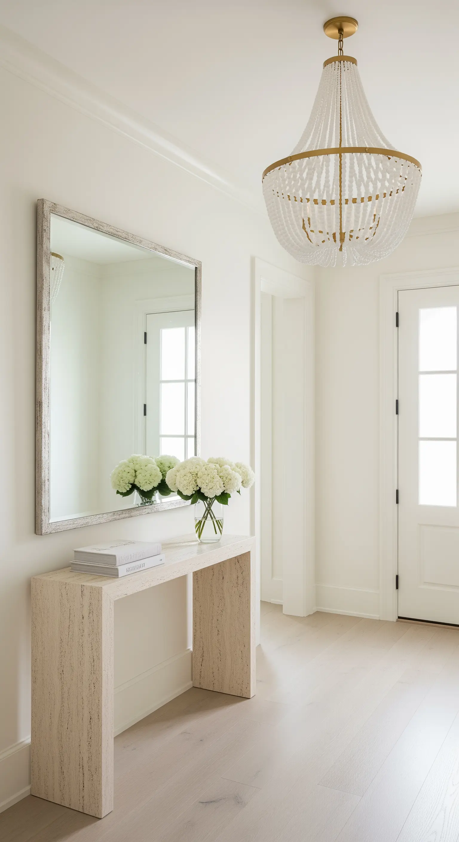 Ingresso total white con consolle in travertino, specchio con cornice in legno e lampadario di perline.