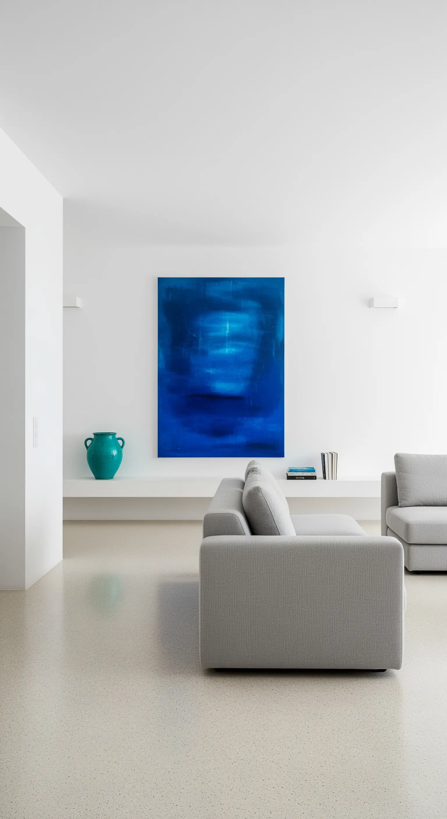 Soggiorno minimalista con un grande quadro astratto blu e un divano grigio.