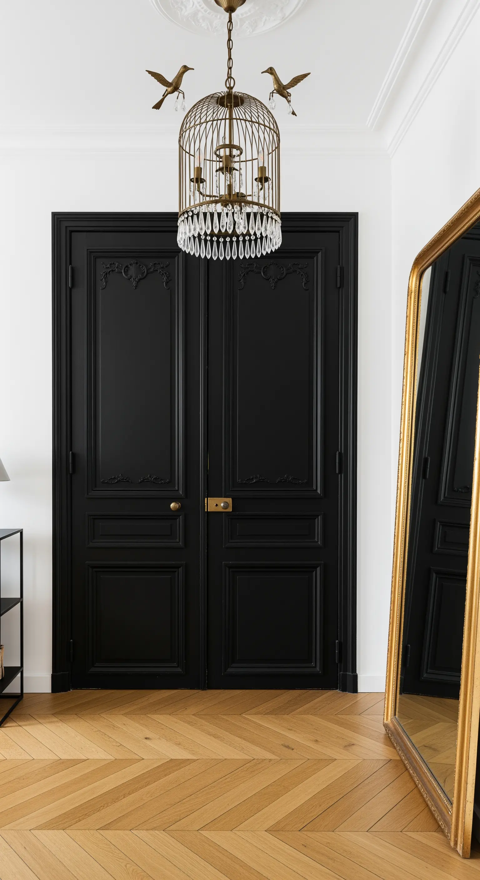 Ingresso parigino con doppie porte nere, parquet a spina di pesce e lampadario a forma di gabbietta.