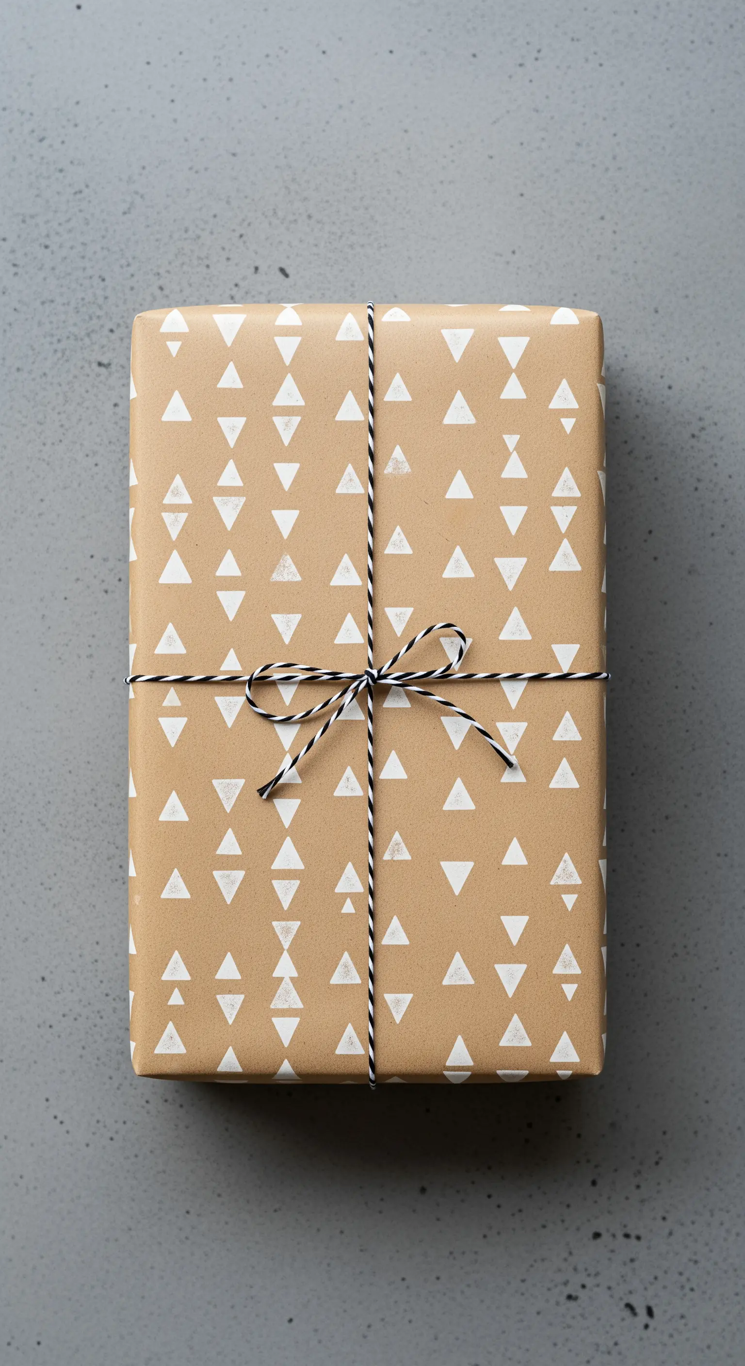 Pacco regalo in carta kraft con triangoli bianchi stampati e spago bianco e nero.