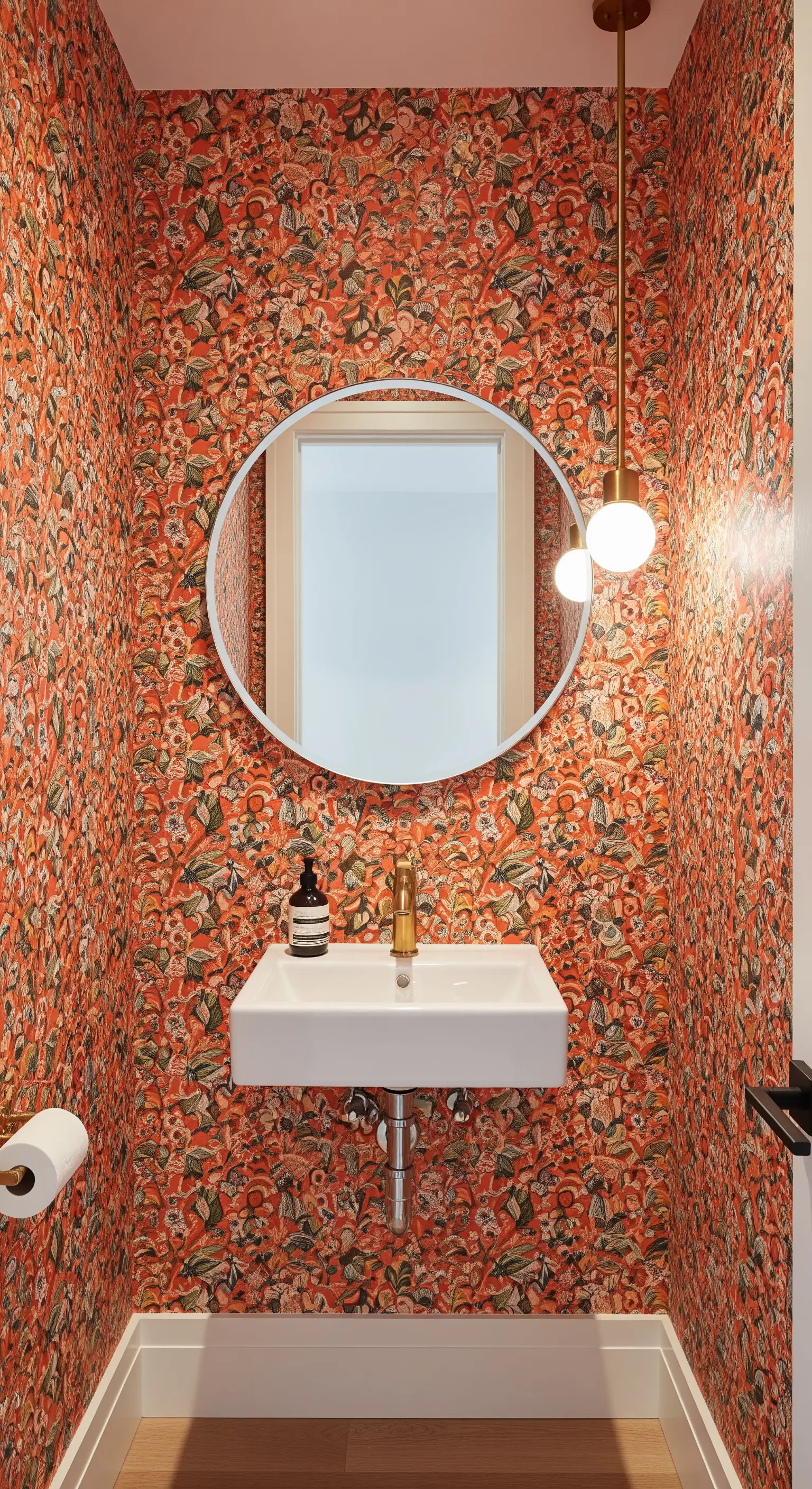 Bagno di servizio con carta da parati arancione a motivi fitti e piccolo lavabo sospeso.