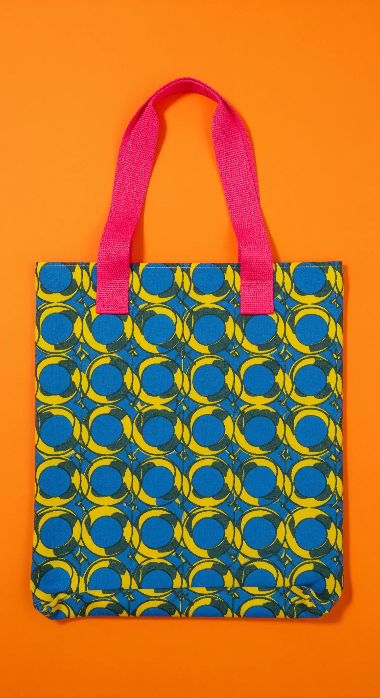 Borsa con motivo geometrico blu e giallo e manici a contrasto in nastro fucsia.