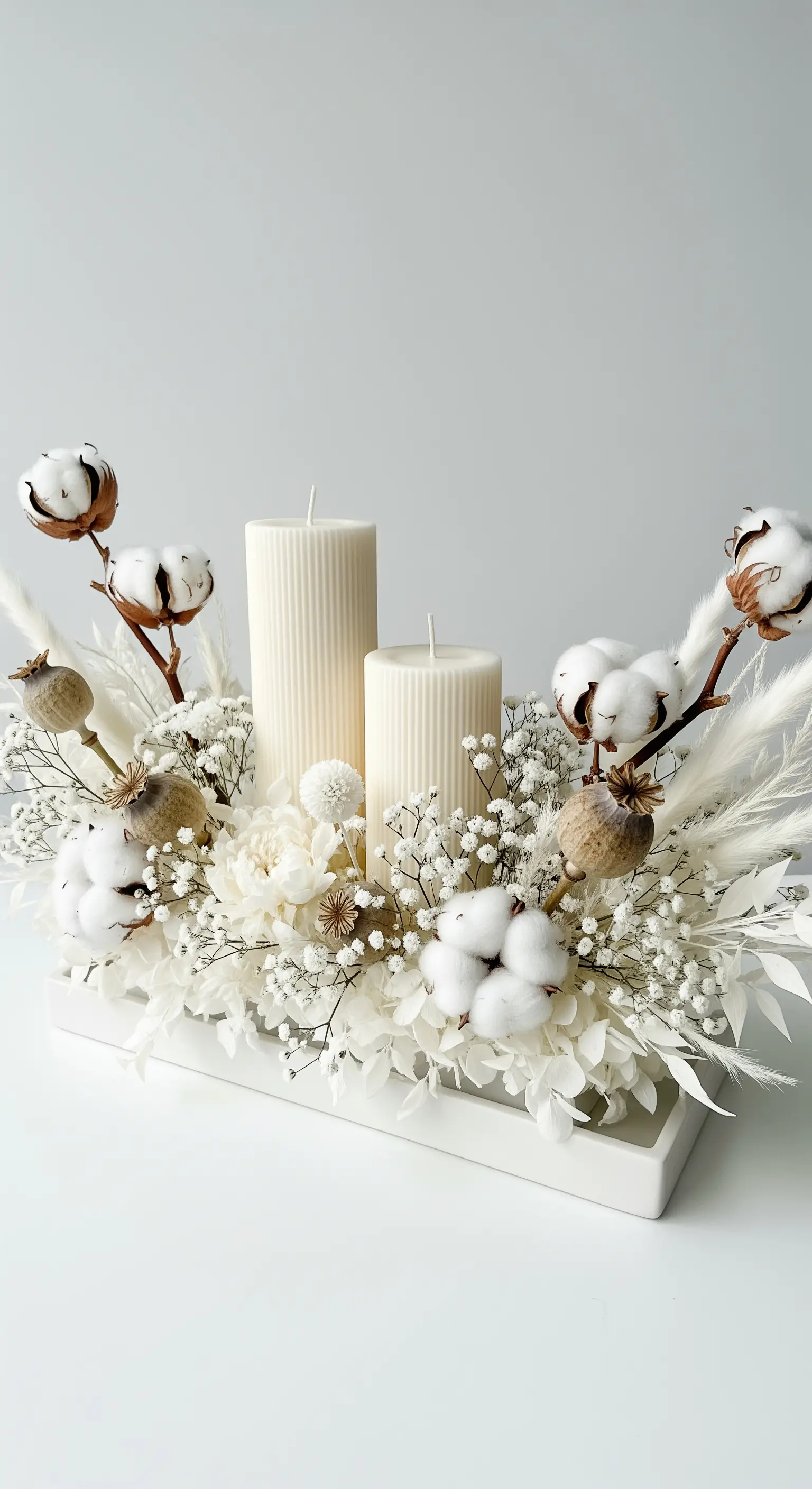 Composizione total white con candele, fiori di cotone, gypsophila e papaveri secchi.