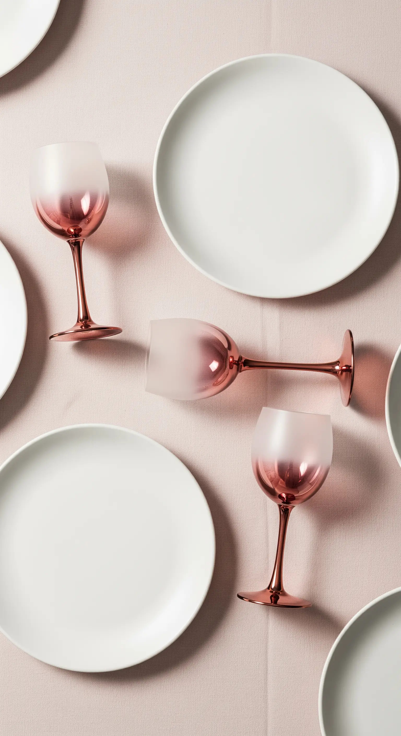 Tavola minimalista con tovaglia rosa pallido, piatti bianchi e calici con stelo rame e coppa satinata