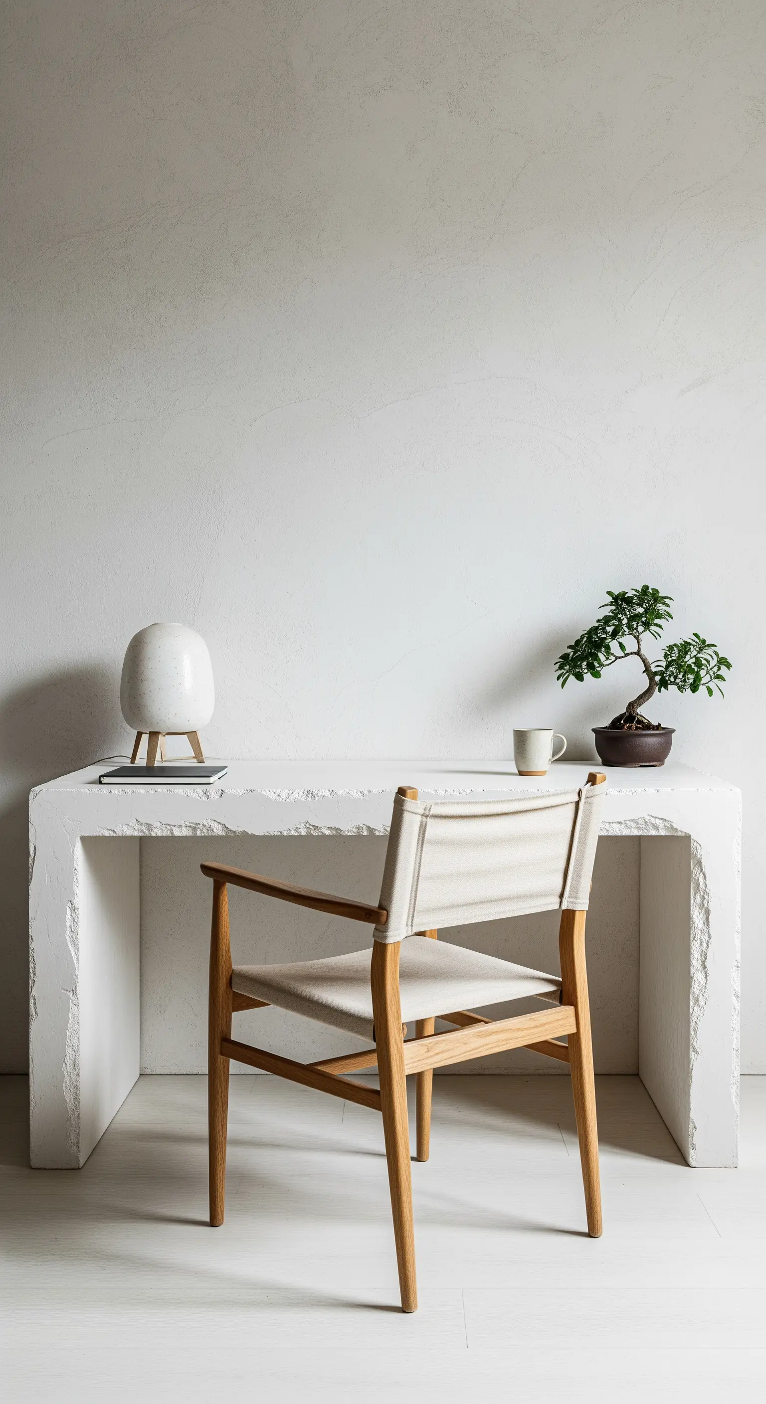Scrivania scultorea in pietra grezza con sedia in legno e tela, e un bonsai.