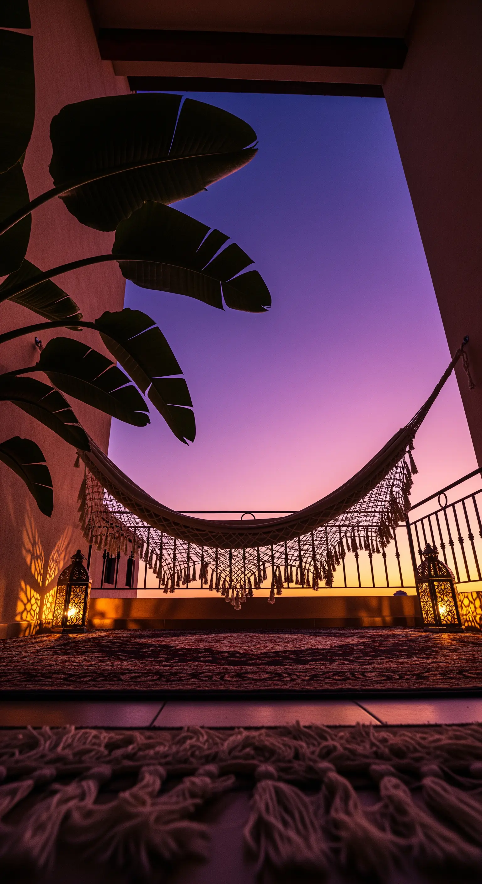 Silhouette di un'amaca su un balcone al tramonto, con due lanterne accese a terra.