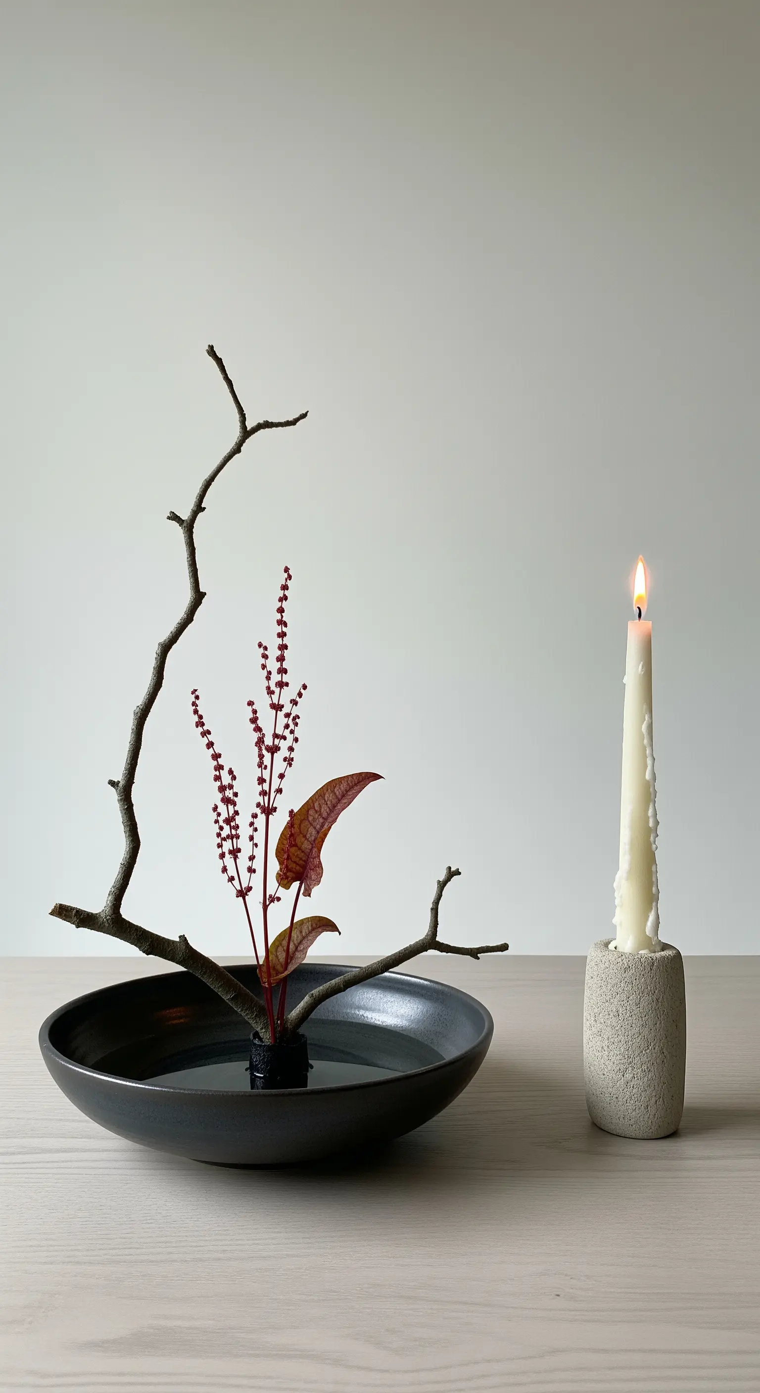 Composizione in stile ikebana con ramo secco, un fiore e una candela.
