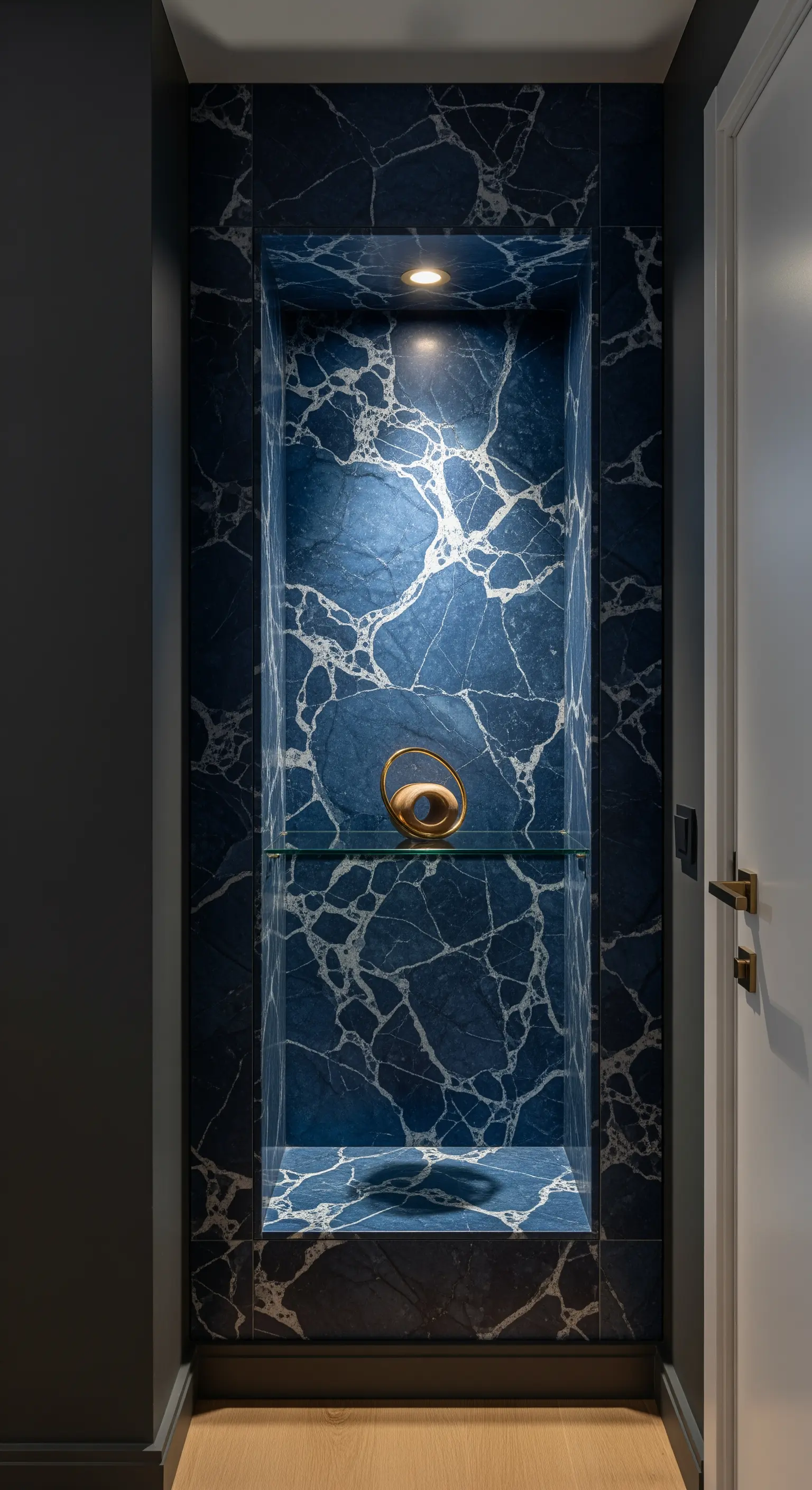 Nicchia illuminata rivestita in marmo blu con un oggetto dorato su mensola di vetro.
